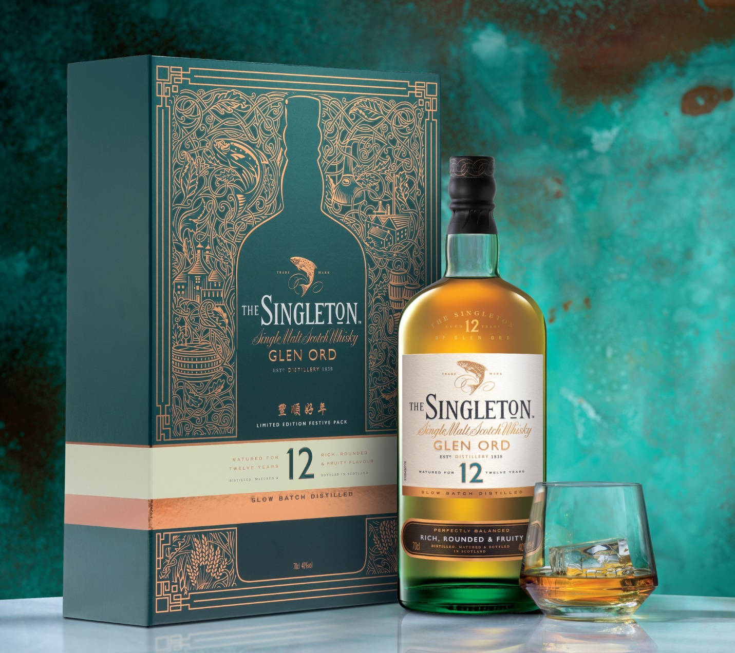 bottle 桌布 壁紙 — 一瓶The Singleton Glen Ord威士忌及其華麗的盒子放在一個有紋理的青綠色背景前，旁邊放著一個加冰的玻璃杯。