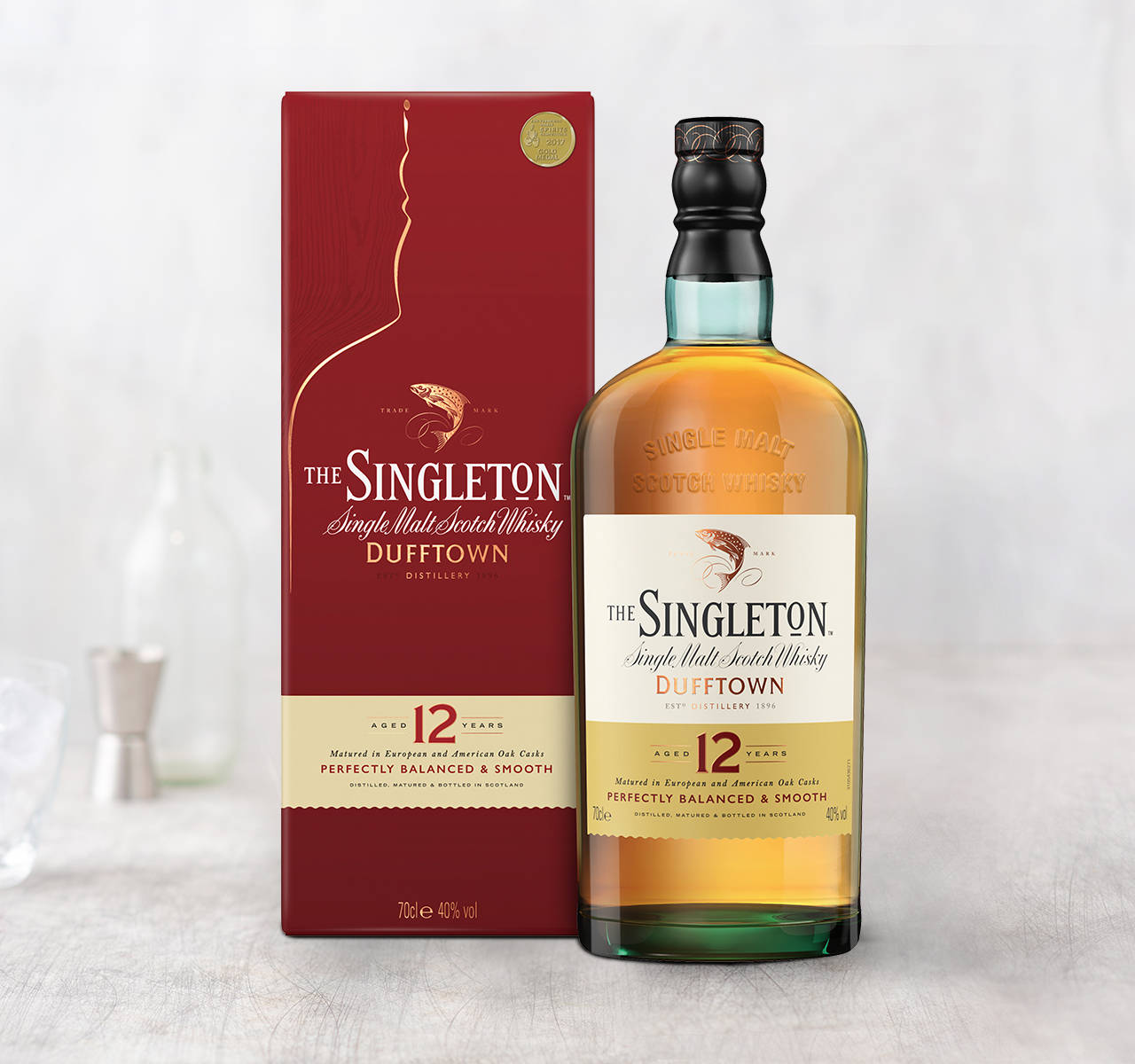 bottle 桌布 壁紙 — 一瓶The Singleton 12年單一麥芽蘇格蘭威士忌，旁邊放著它的紅色盒子，在淺色木質表面上，背景有吧檯工具，呈現柔和焦點。