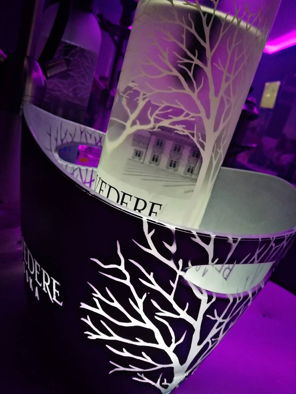 Drink 桌布 壁紙 — 一瓶VEDERE伏特加酒放在一個相配的冰桶中，兩者都飾有在紫色環境光下發光的白色樹木剪影。