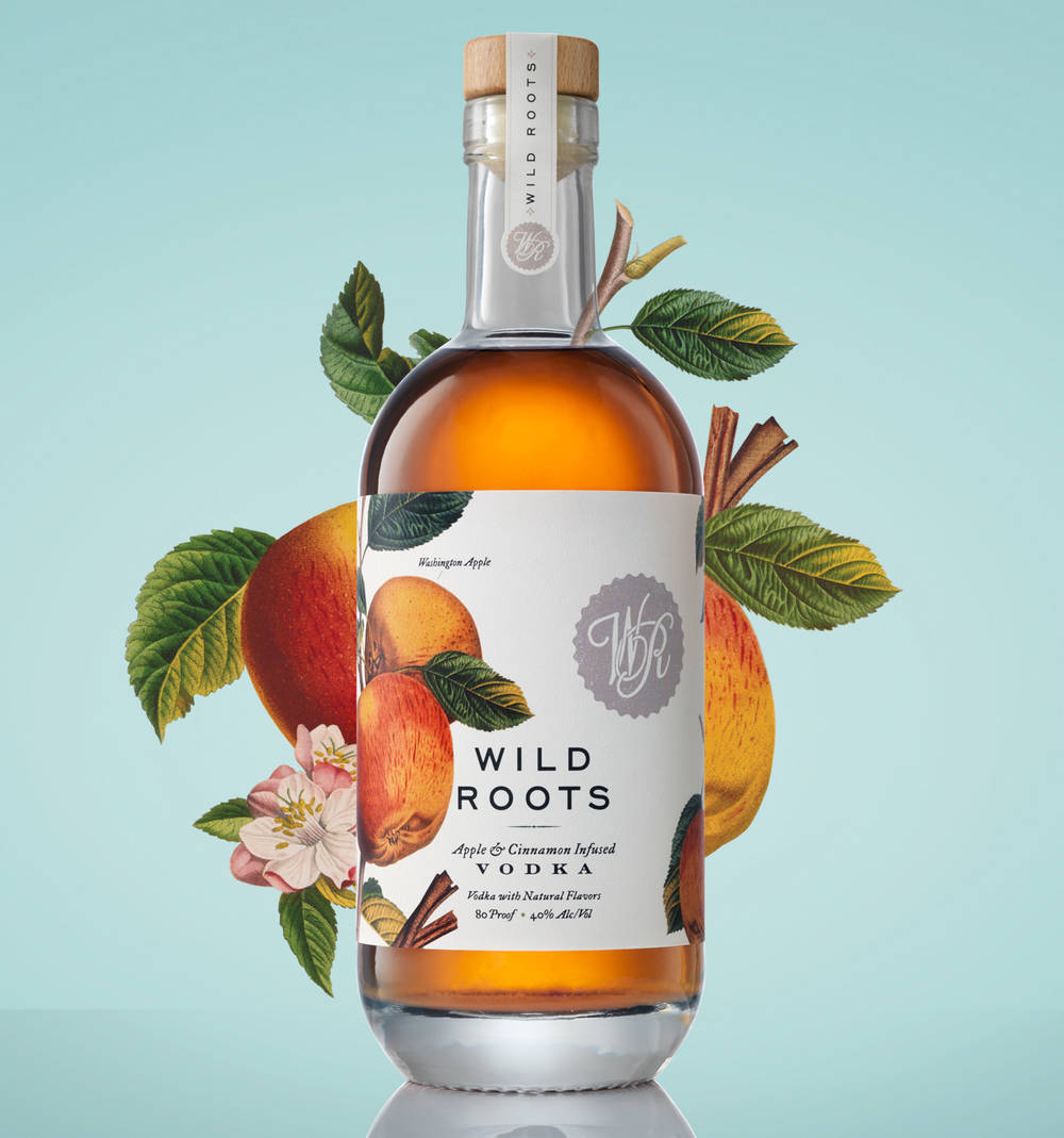 bottle 桌布 壁紙 — 一瓶Wild Roots蘋果肉桂伏特加，周圍環繞著新鮮水果葉和肉桂棒，背景是柔和的青綠色。