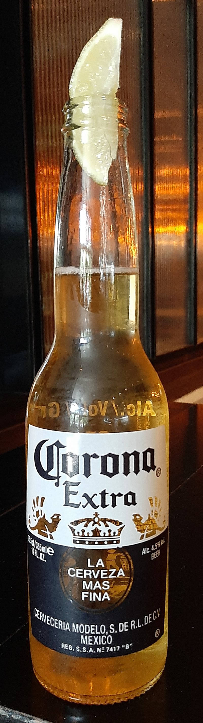 corona 桌布 壁紙 — 一瓶冰涼的Corona Extra啤酒，瓶口放著一片萊姆，在深色木質背景下溫暖地發光。