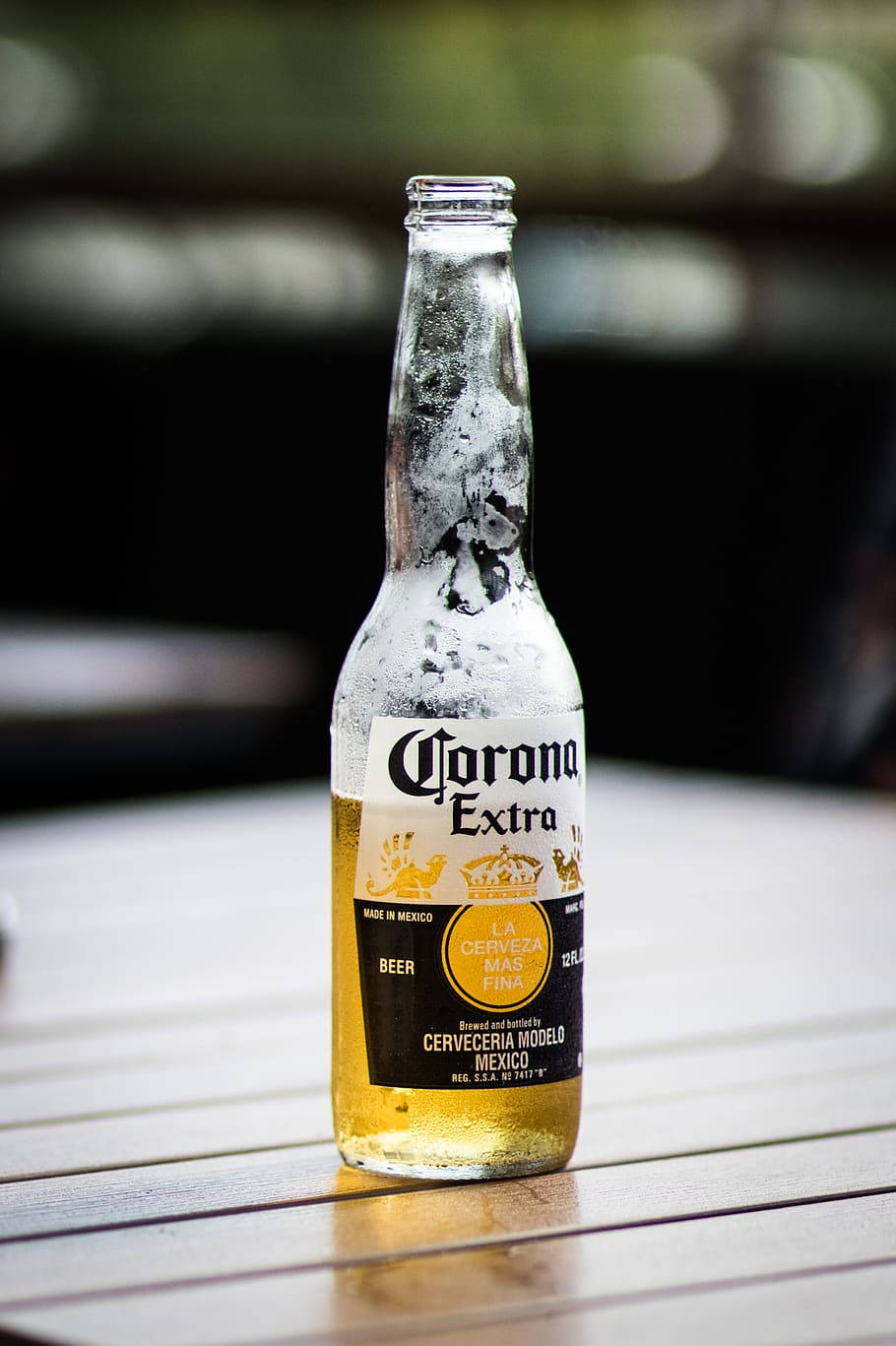 corona 桌布 壁紙 — 一瓶冰涼的Corona Extra啤酒，帶有水珠，放在戶外的木桌上。