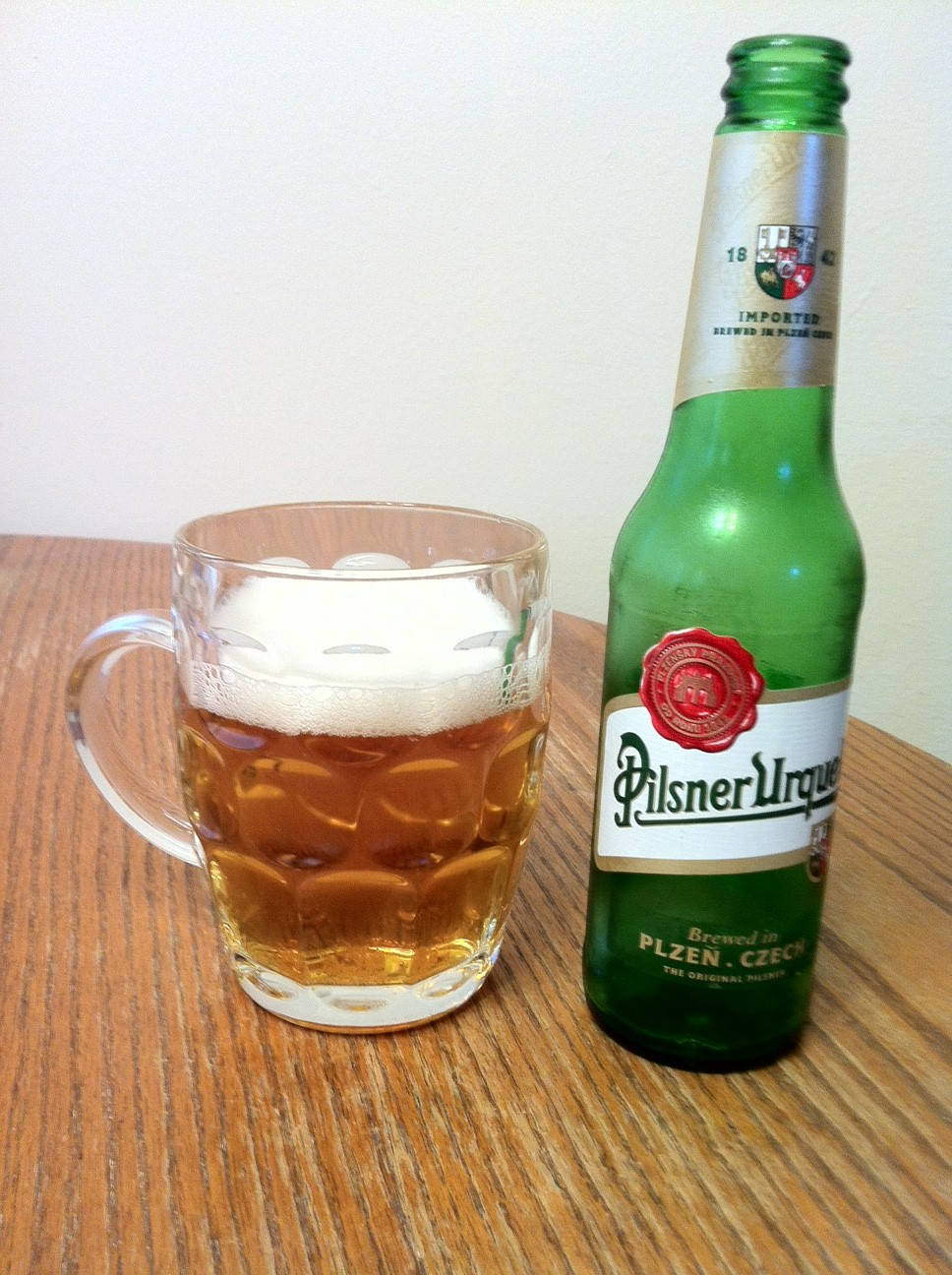Beer Bottle 桌布 壁紙 — 一瓶冰涼的Pilsner Urquell啤酒和一個起泡的玻璃杯放在木桌上，背景是素牆。