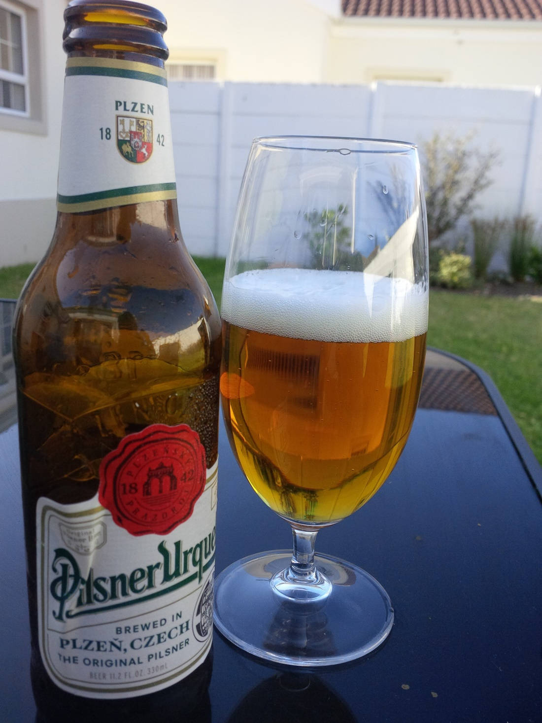 glass 桌布 壁紙 — 一瓶冰涼的Pilsner Urquell啤酒和一個滿杯泡沫的玻璃杯放在戶外的深色桌子上。