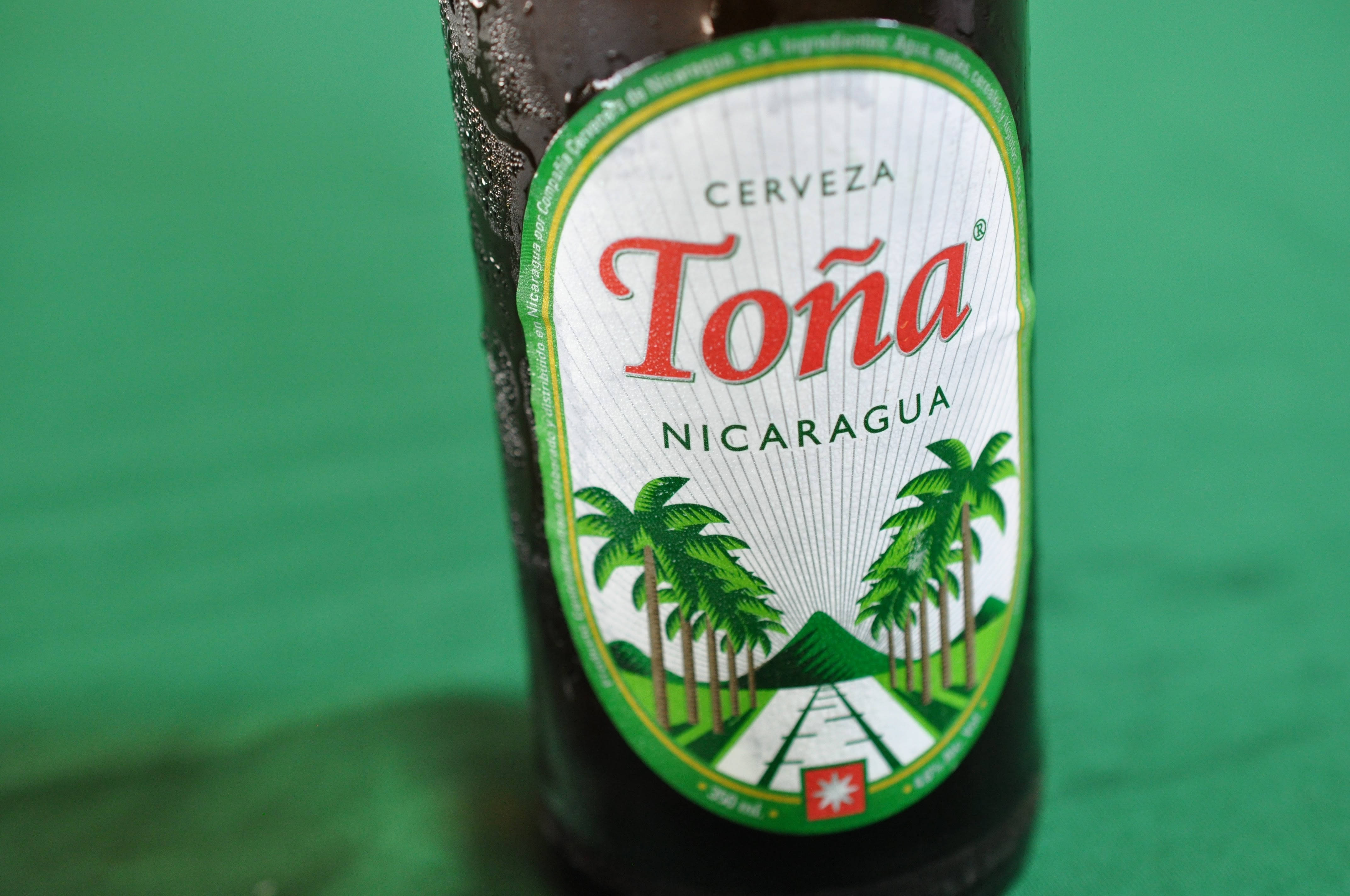 Nicaragua 桌布 壁紙 — 一瓶冰涼的Toná啤酒，帶有冷凝水滴，放在純綠色背景前。