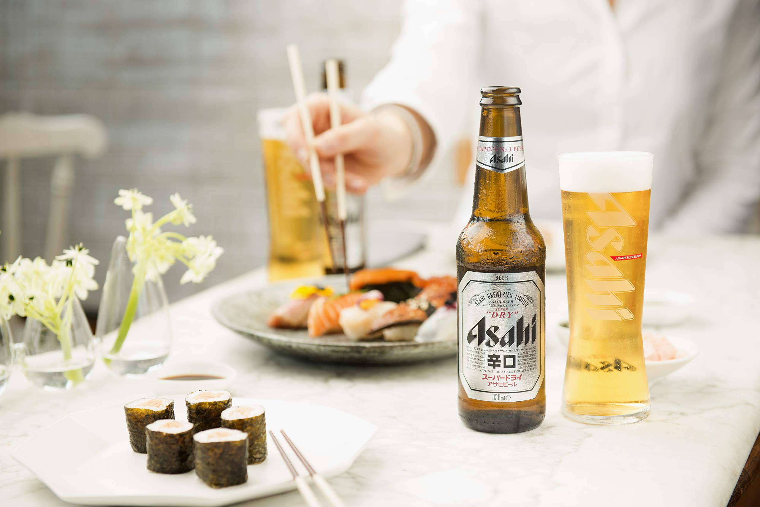 Beer 桌布 壁紙 — 一瓶冰涼的朝日啤酒和玻璃杯放在大理石桌上，旁邊有壽司卷和生魚片，桌上還有白色花朵。