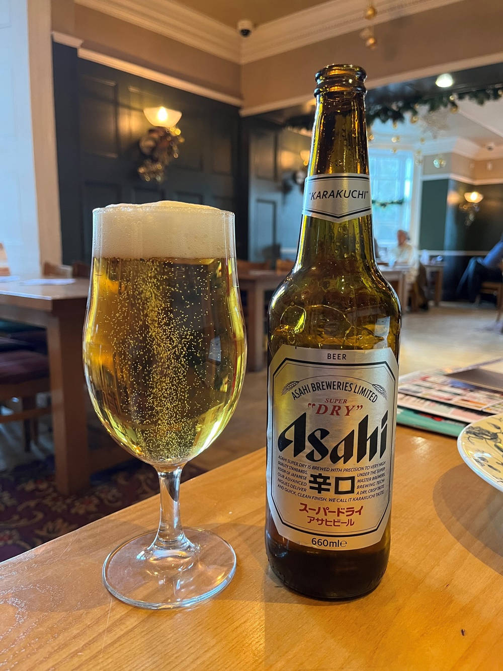 alcohol 桌布 壁紙 — 一瓶冰涼的朝日超乾啤酒和一杯金色氣泡啤酒放在舒適酒吧的木桌上。