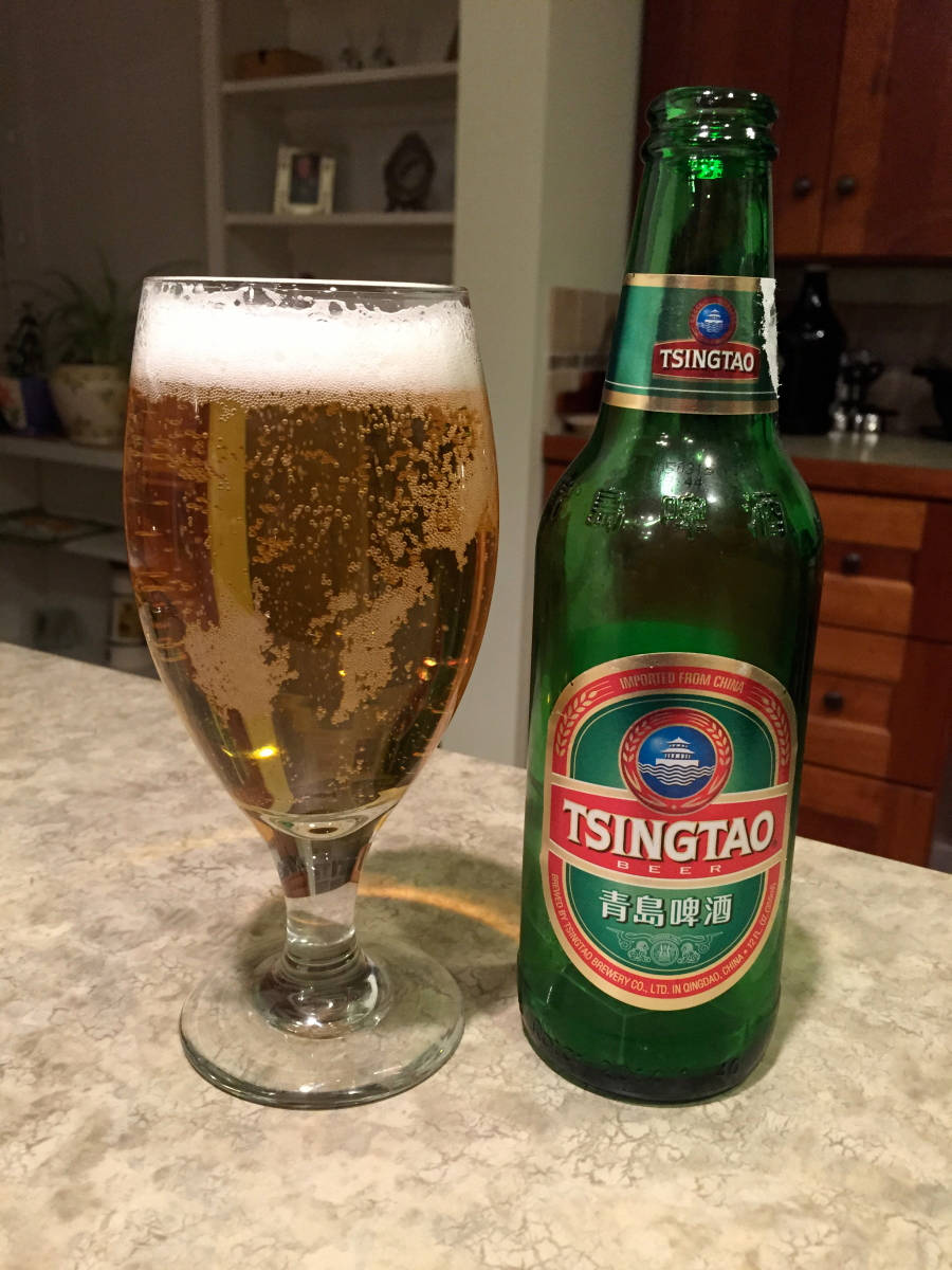 booze 桌布 壁紙 — 一瓶冰涼的青島啤酒和帶有泡沫的酒杯放在廚房檯面上，在溫暖的室內燈光下。