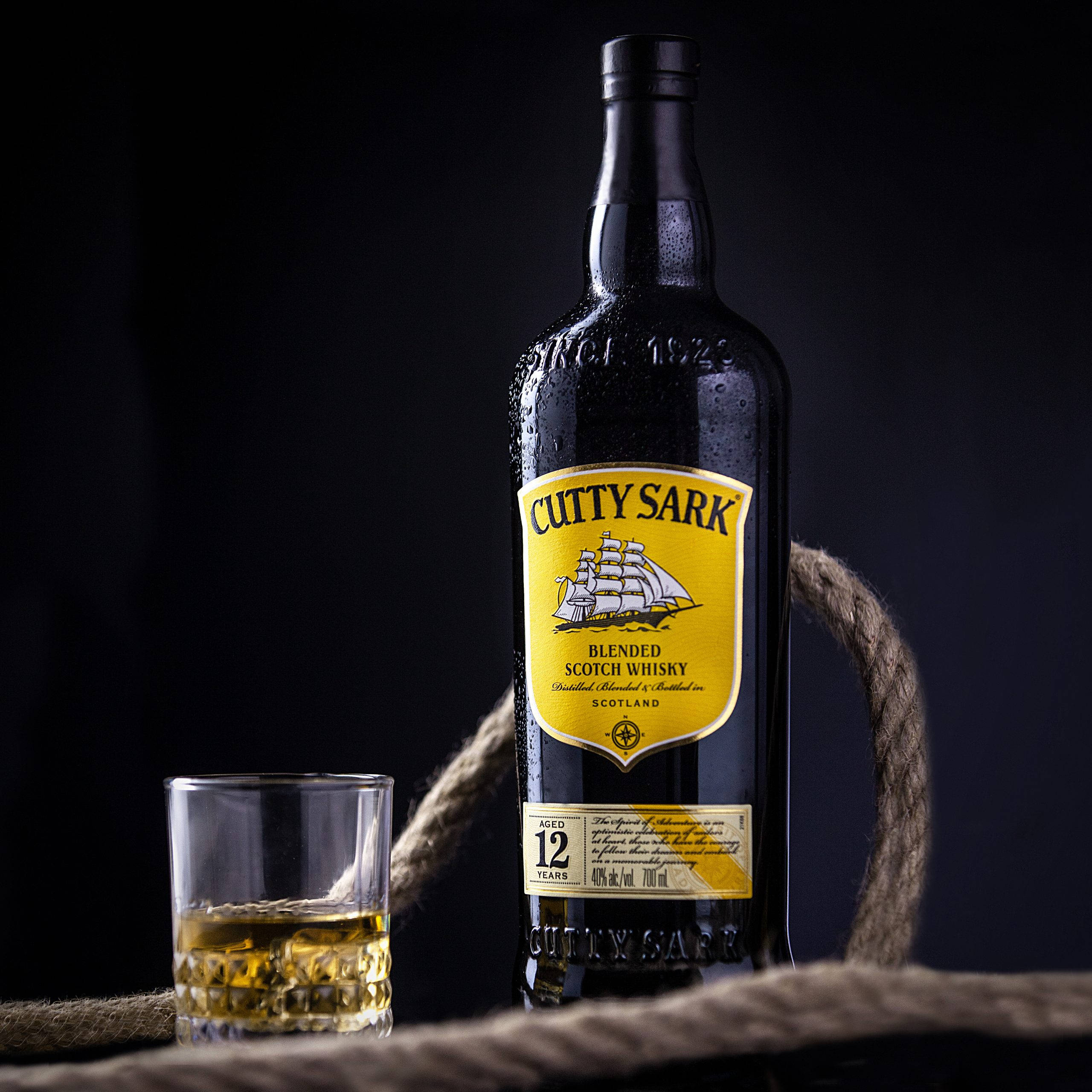 alcohol 桌布 壁紙 — 一瓶冰鎮的Cutty Sark威士忌，旁邊放著一杯琥珀色液體和一條粗繩，背景深色。