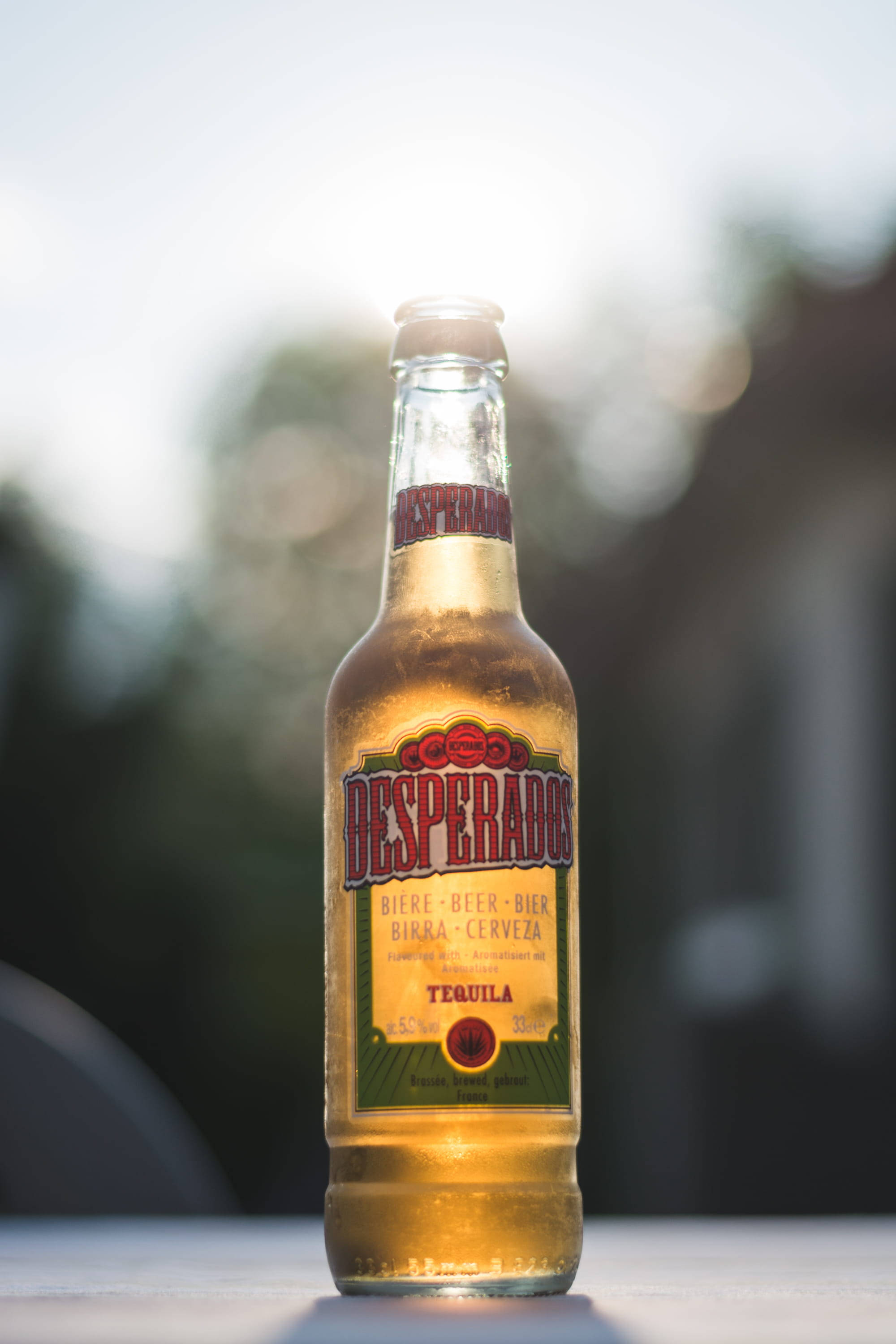 glass 桌布 壁紙 — 一瓶冰鎮的Desperados龍舌蘭啤酒在柔和日光下閃耀，背景是模糊的戶外景色。