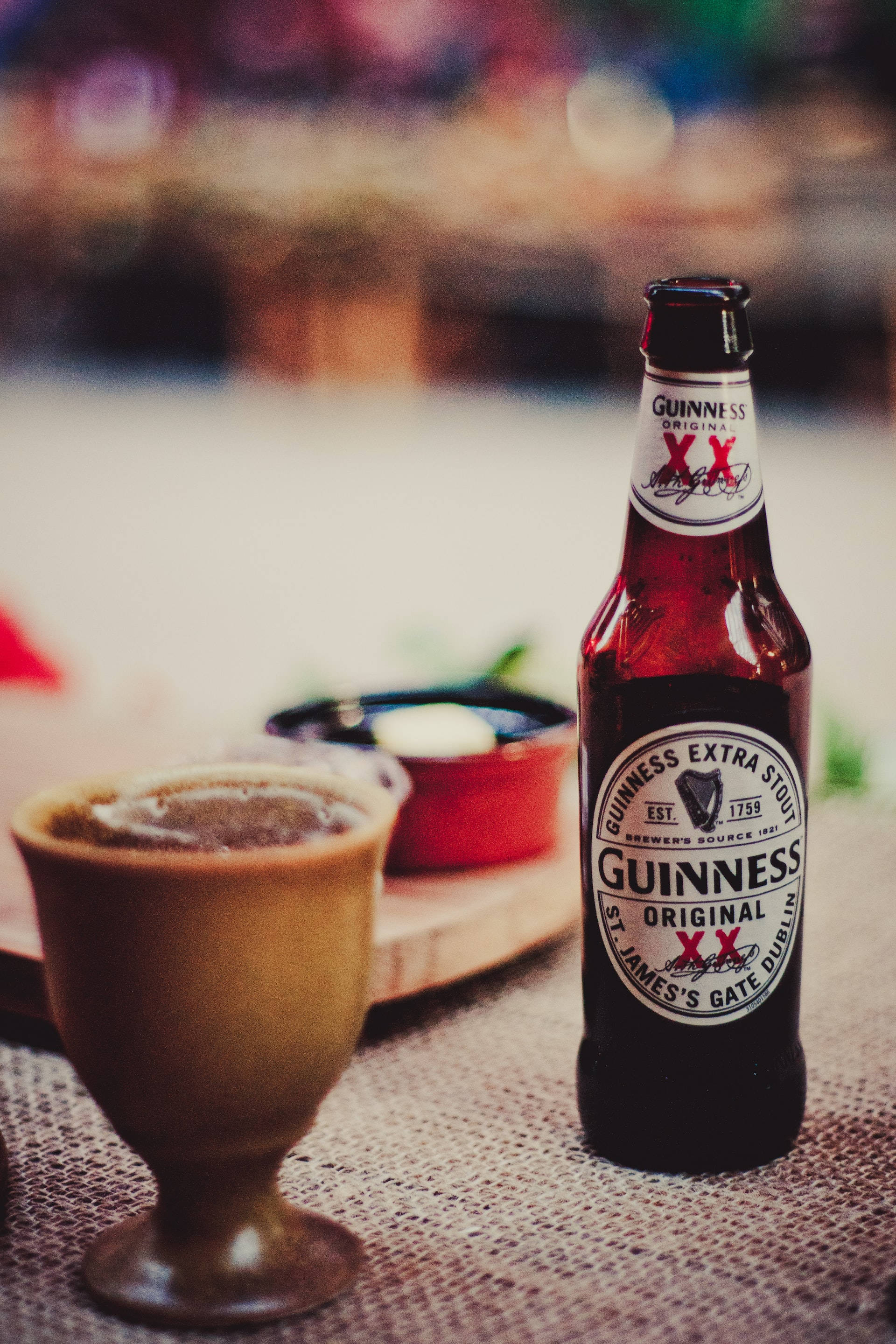 Beer 桌布 壁紙 — 一瓶冰鎮的健力士黑啤酒連同一個裝滿的玻璃杯放在溫暖燈光酒吧的紋理桌布上。