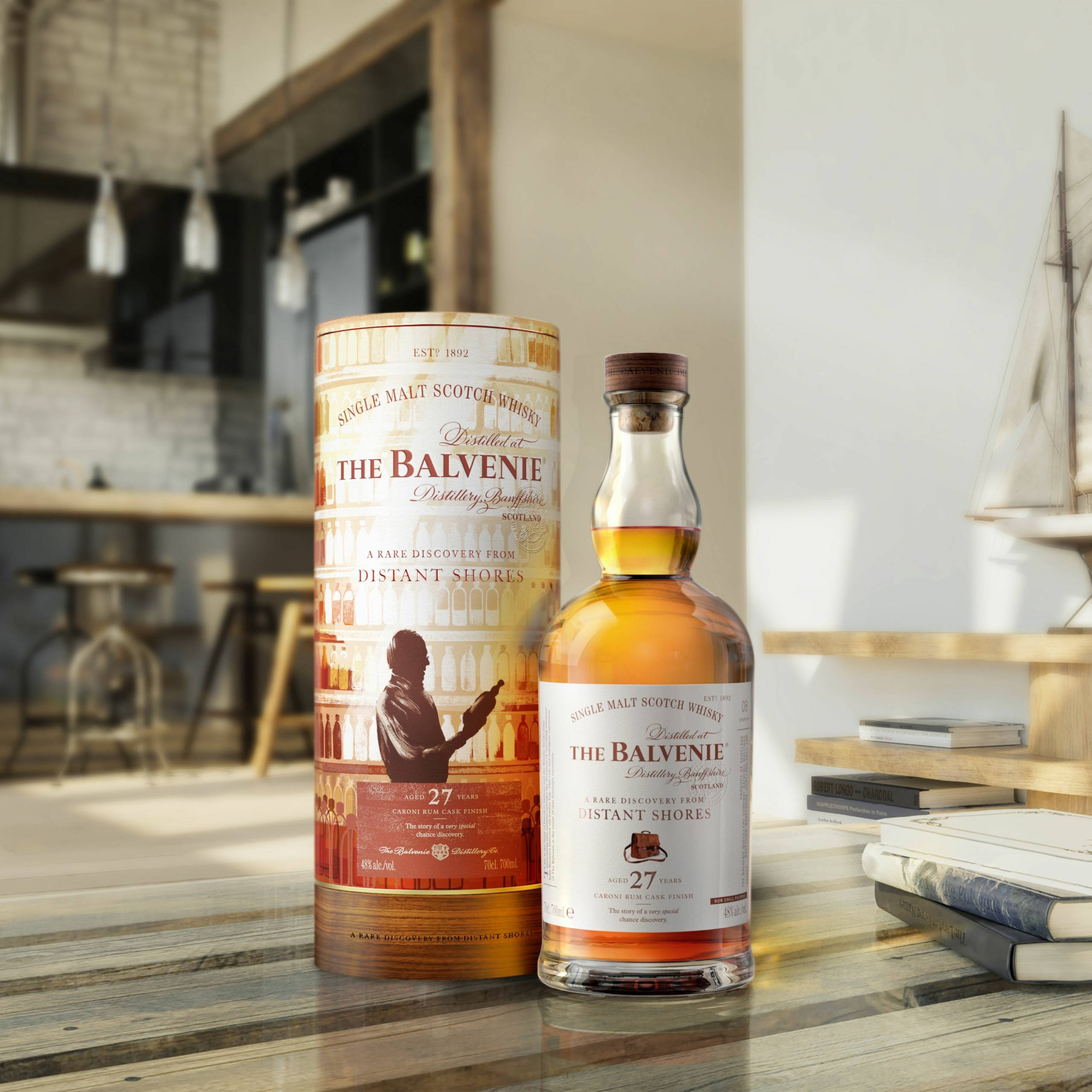 飲料 桌布 壁紙 — 一瓶和一支The Balvenie 27年威士忌放在現代廚房的木桌上，附近有帆船模型和書籍。