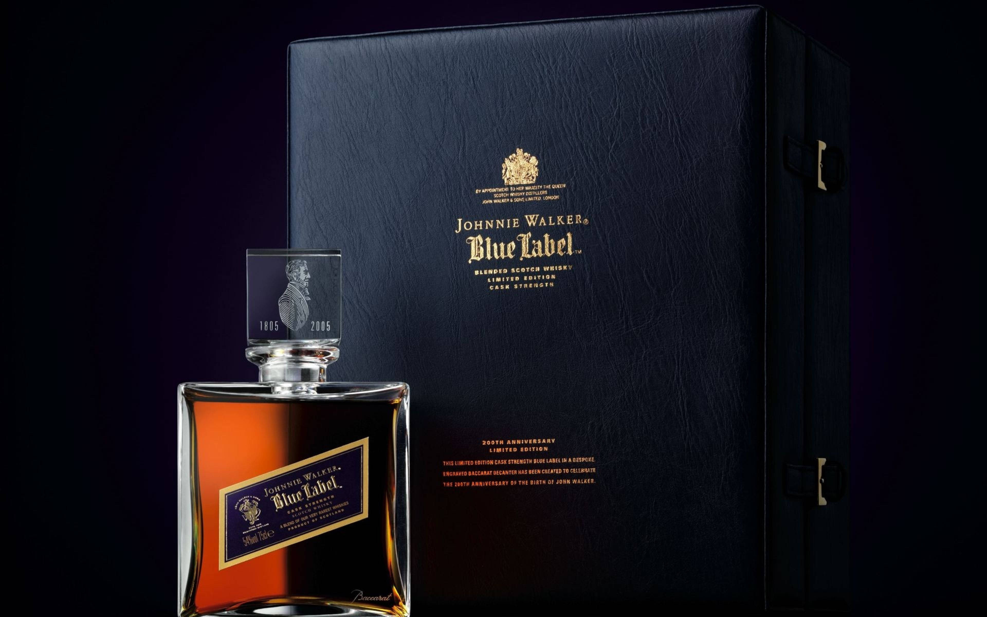 飲料 桌布 壁紙 — 一瓶奢華的Johnnie Walker Blue Label威士忌在戲劇性的工作室燈光下，在其優雅的黑色禮盒旁閃閃發光。