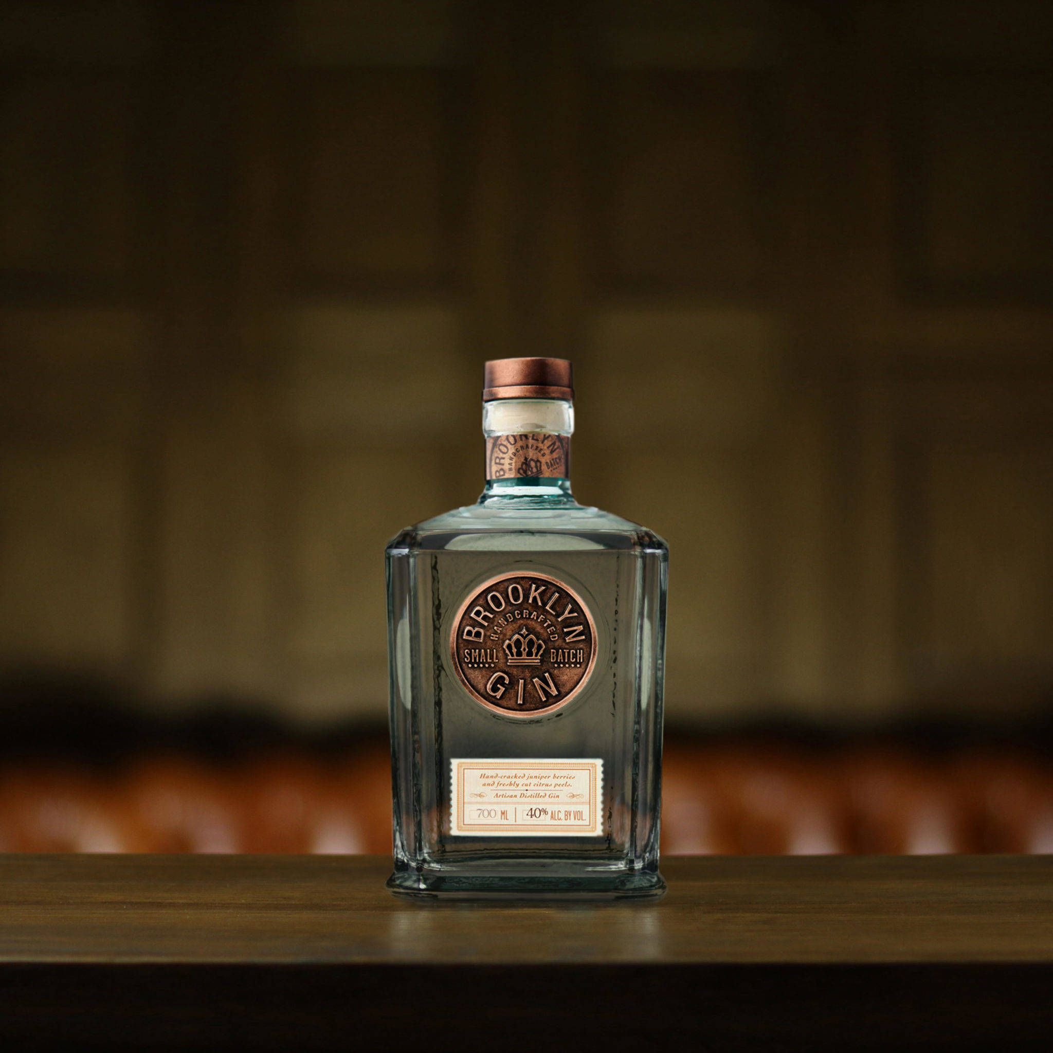 Gin 桌布 壁紙 — 一瓶布魯克林小批量琴酒的透明玻璃瓶放在木吧檯中央，背景是模糊的皮革卡座。