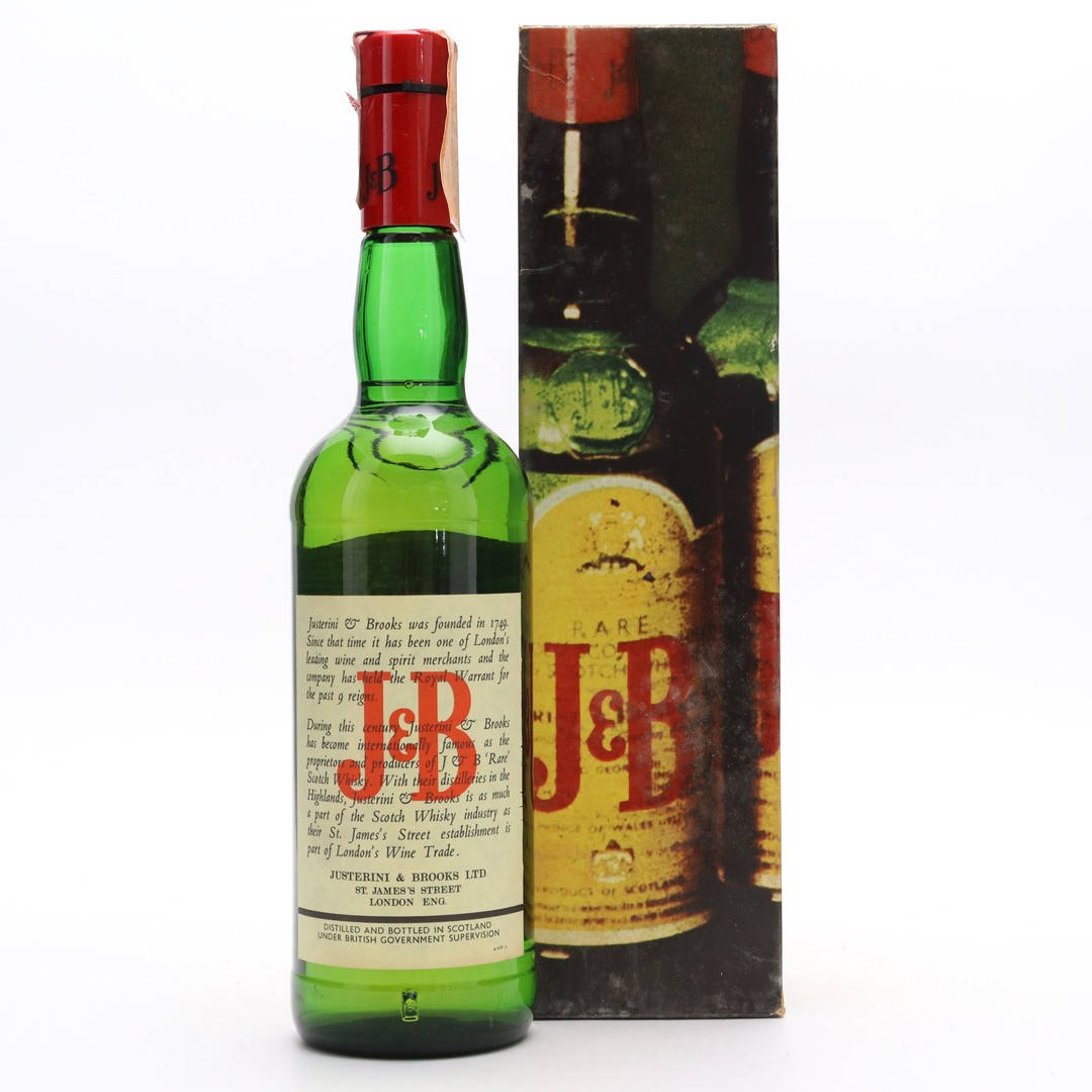 drinks 桌布 壁紙 — 一瓶帶有紅色箔蓋的復古綠色玻璃瓶J&B Rare蘇格蘭威士忌，站在其老化的紙板箱旁邊，背景為白色。