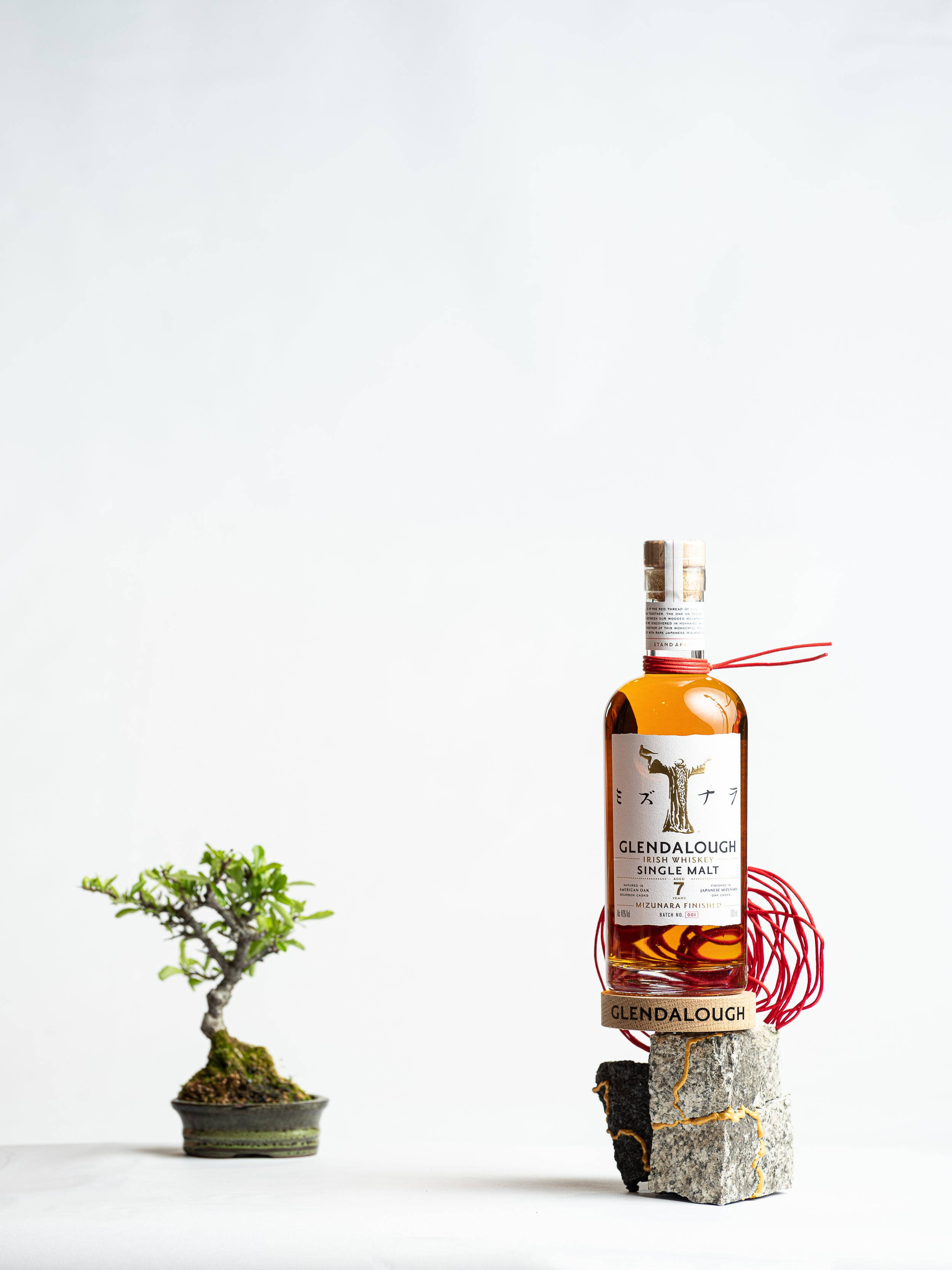 Whiskey 桌布 壁紙 — 一瓶帶有紅色鐵線藝術的格蘭達洛威士忌，放在極簡白色表面的盆景樹旁。