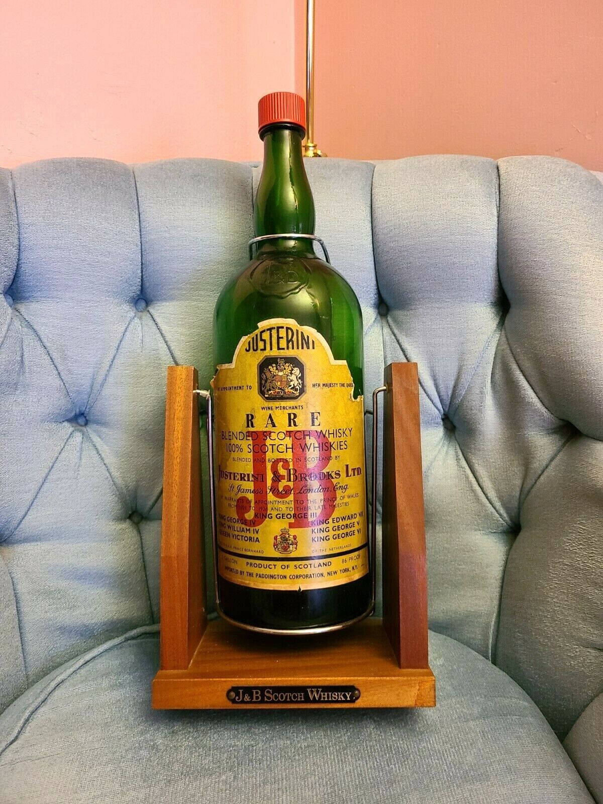 drinks 桌布 壁紙 — 一瓶復古綠色Justerini & Brooks稀有調和蘇格蘭威士忌，優雅地放置在淺藍色簇絨沙發上的木架上，背景是柔和的粉紅色牆壁。