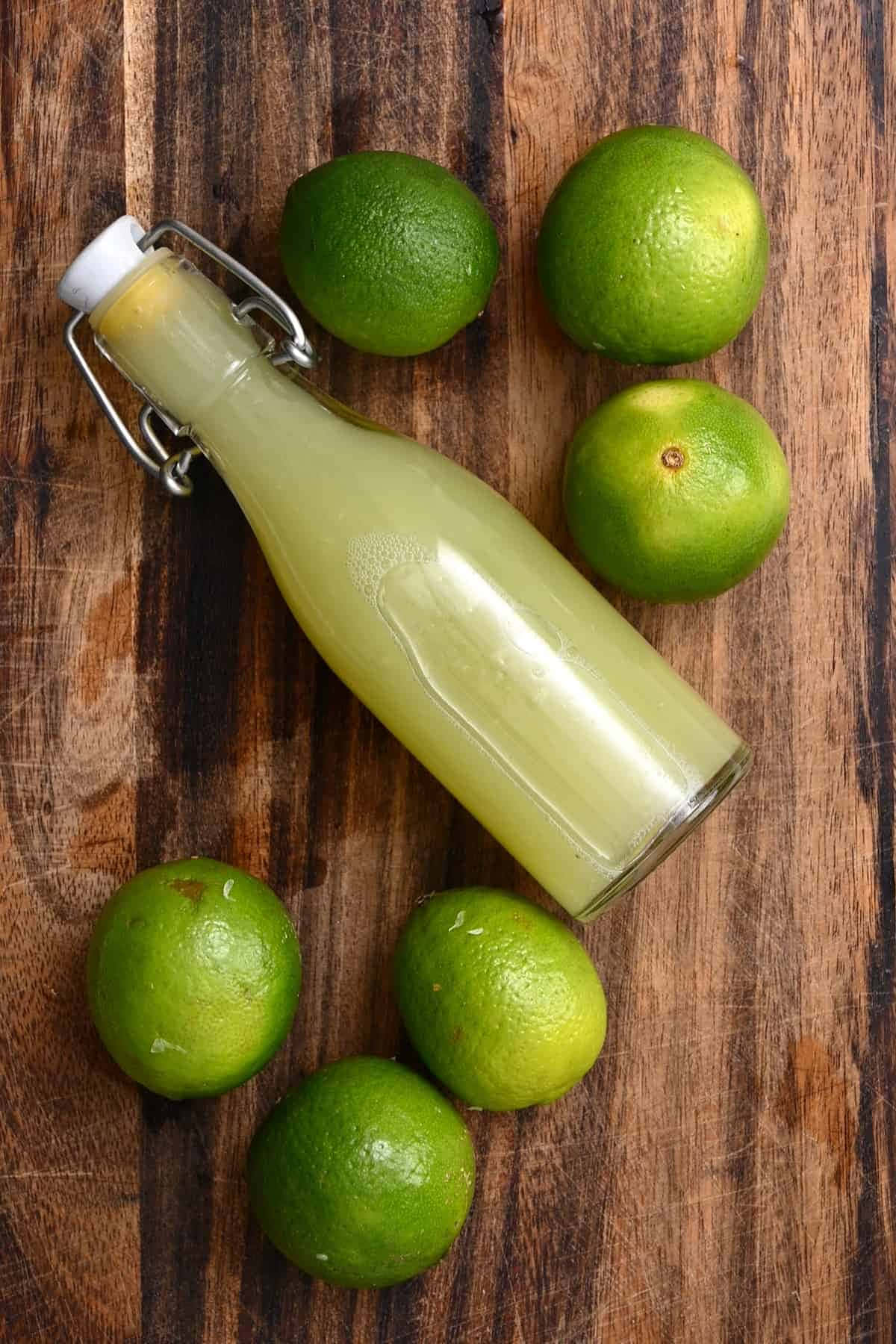 Lime 桌布 壁紙 — 一瓶新鮮萊姆汁的玻璃瓶放在一塊質樸的木板上，周圍環繞著整個綠色萊姆。
