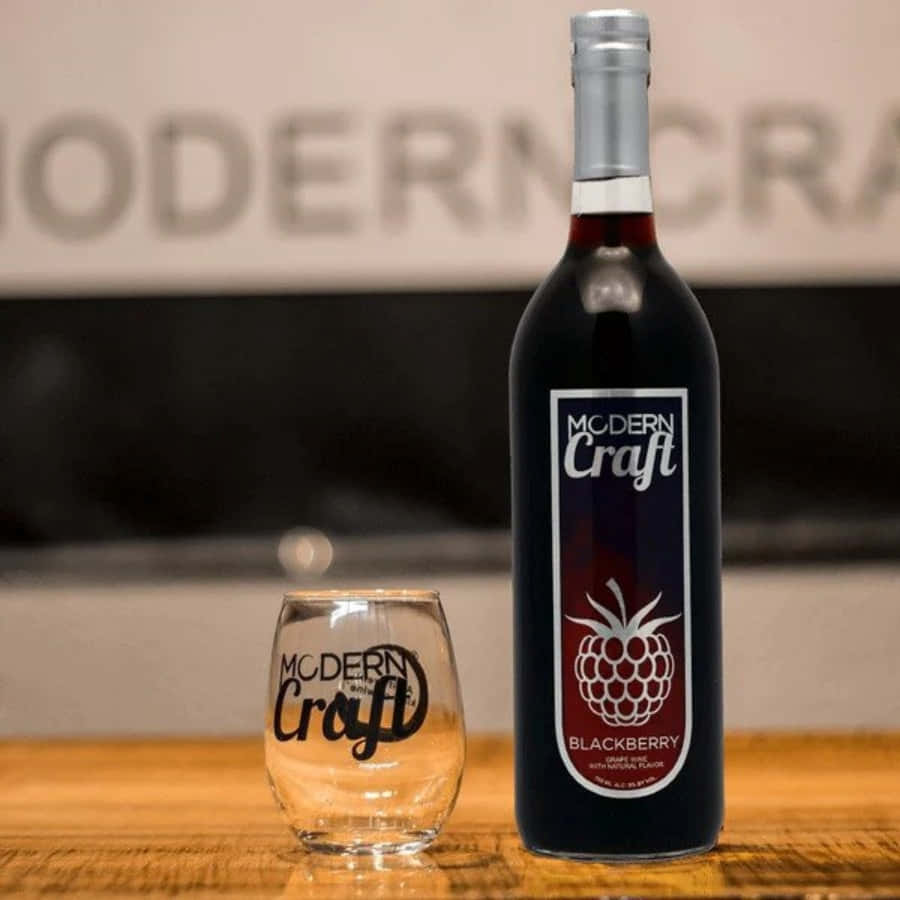 Blackberry Wine 桌布 壁紙 — 一瓶時尚的Modern Craft黑莓酒黑色酒瓶，旁邊放著一個相配的品牌酒杯，放在溫暖的木桌上。