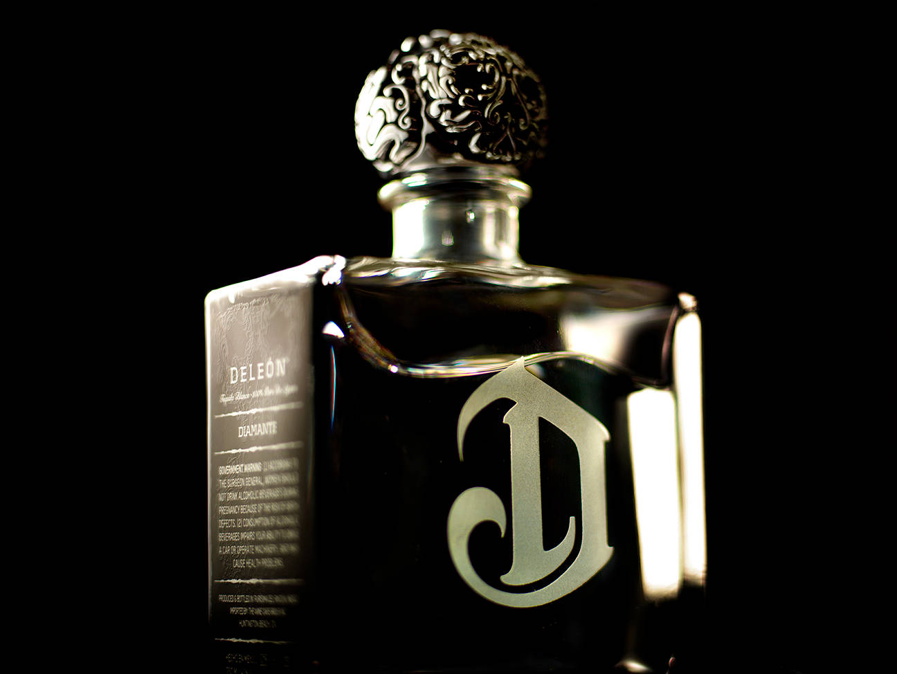 bottle 桌布 壁紙 — 一瓶時尚的黑色Deleón Diamond龍舌蘭酒，帶有華麗的銀色瓶蓋和標誌，在純黑色背景上閃耀。
