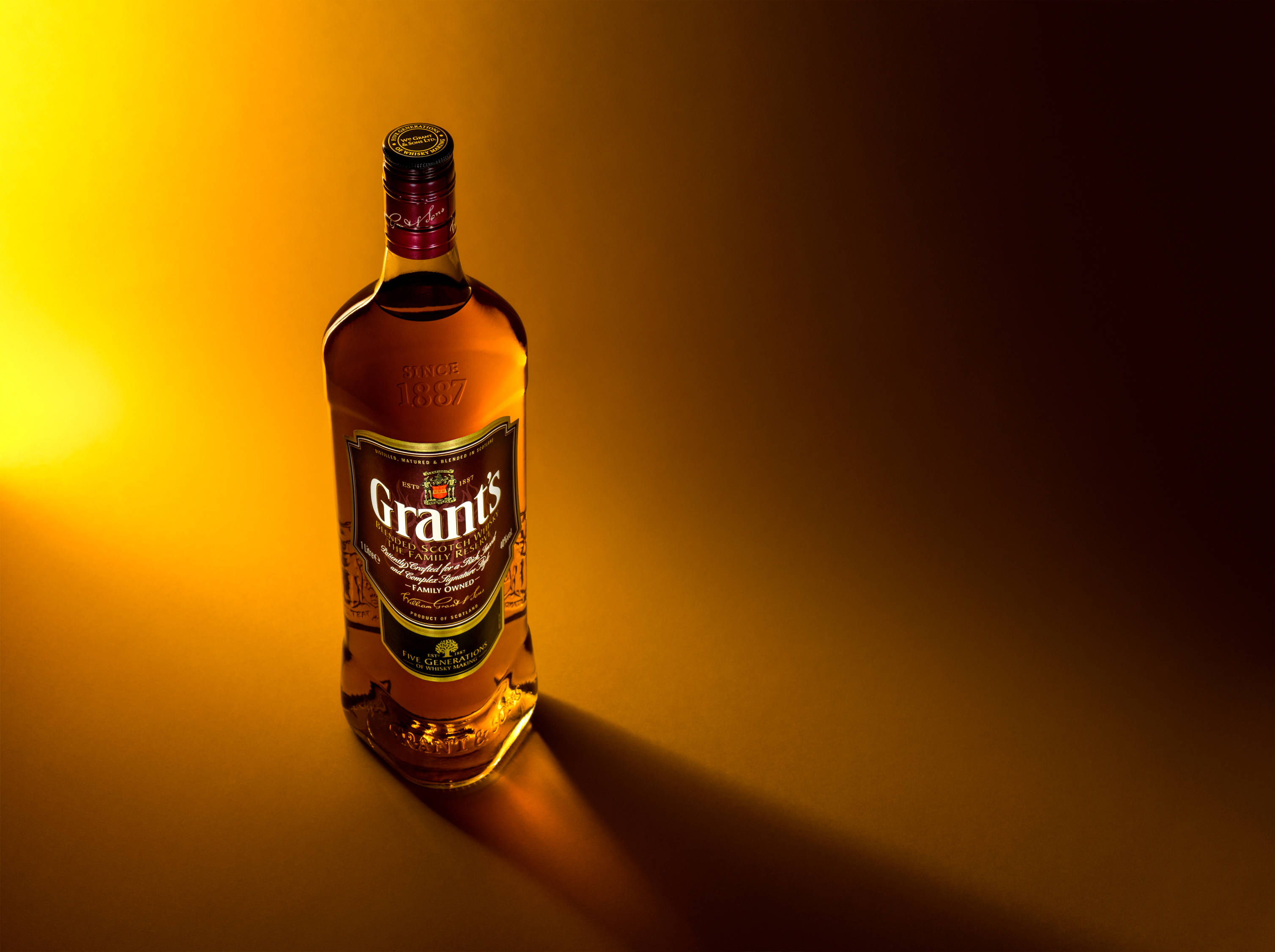 alcohol 桌布 壁紙 — 一瓶格蘭威士忌在金色光線下溫暖地發光，背景由黃色漸變至黑色。
