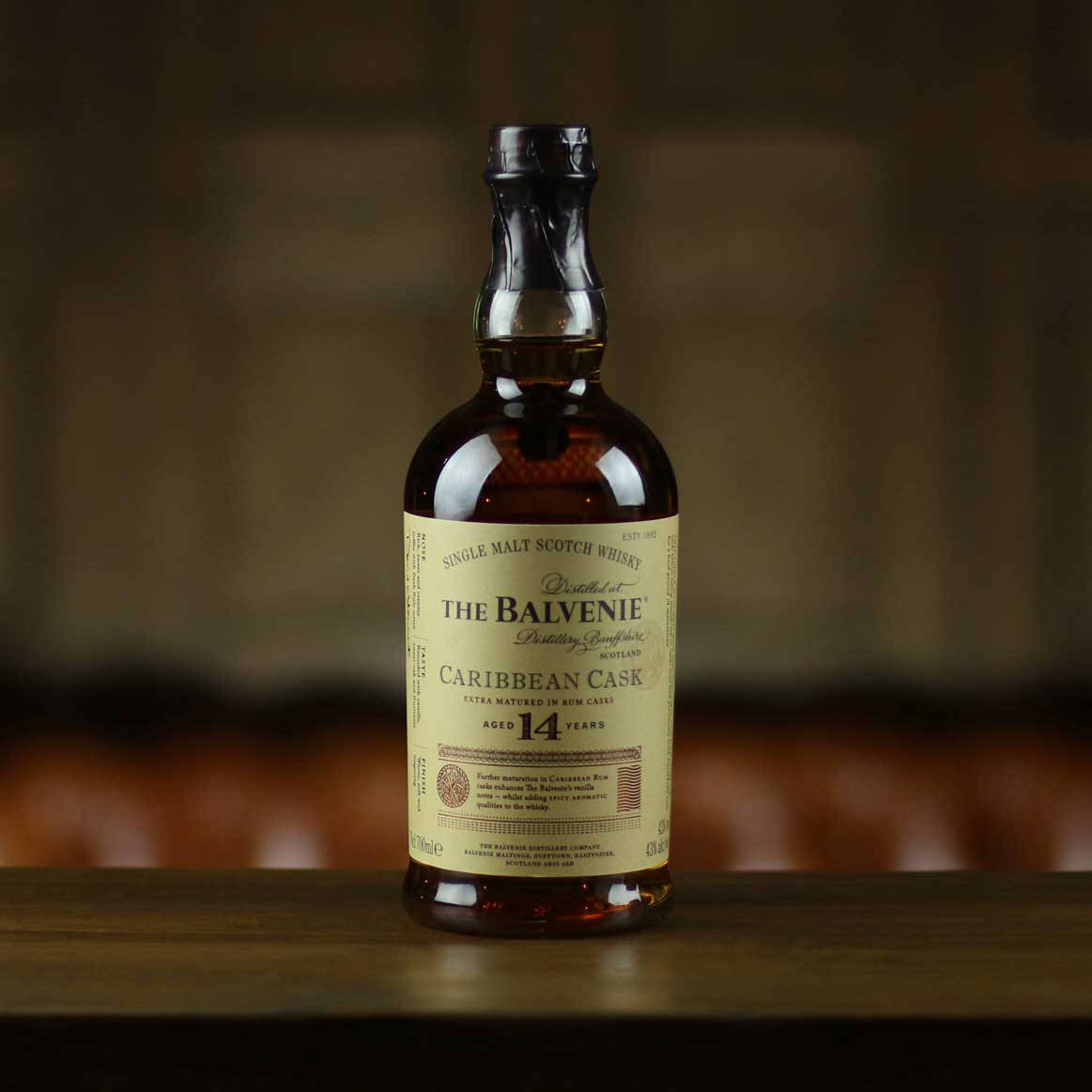 Drink 桌布 壁紙 — 一瓶標有 The Balvenie Caribbean Cask 14 年陳釀的單一麥芽蘇格蘭威士忌，居中放置在木質表面上，背景模糊且色調溫暖。