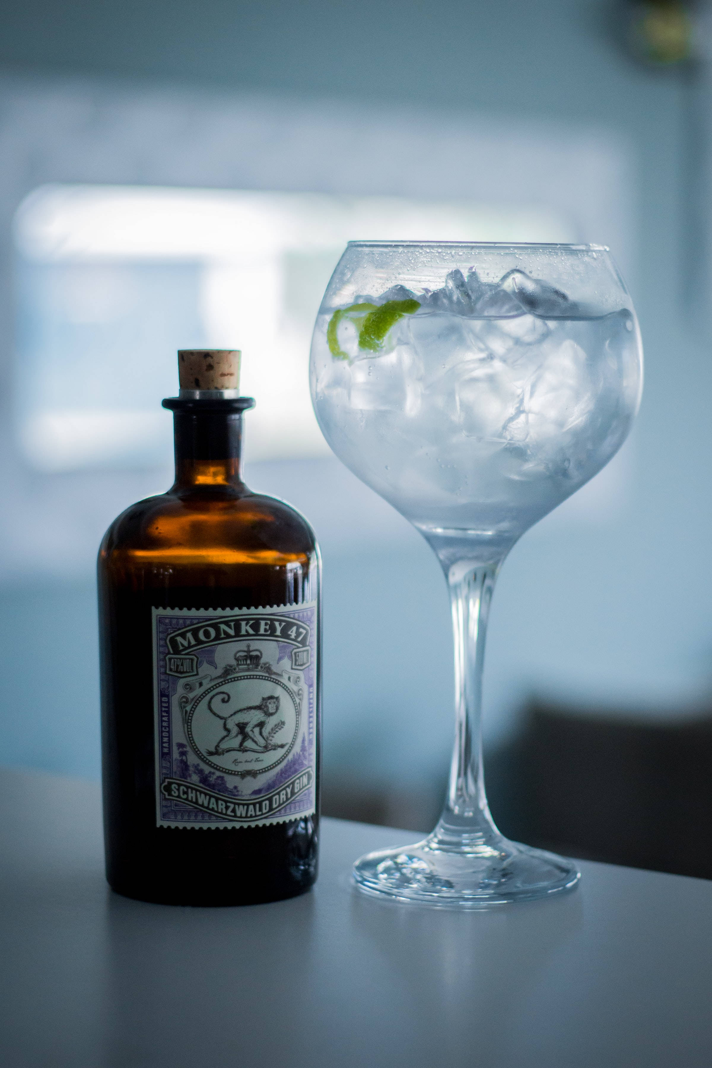 drinks 桌布 壁紙 — 一瓶深琥珀色的Monkey 47琴酒放在一個時尚的檯面上，旁邊是一個裝滿冰塊和萊姆角的琴酒通寧酒杯。