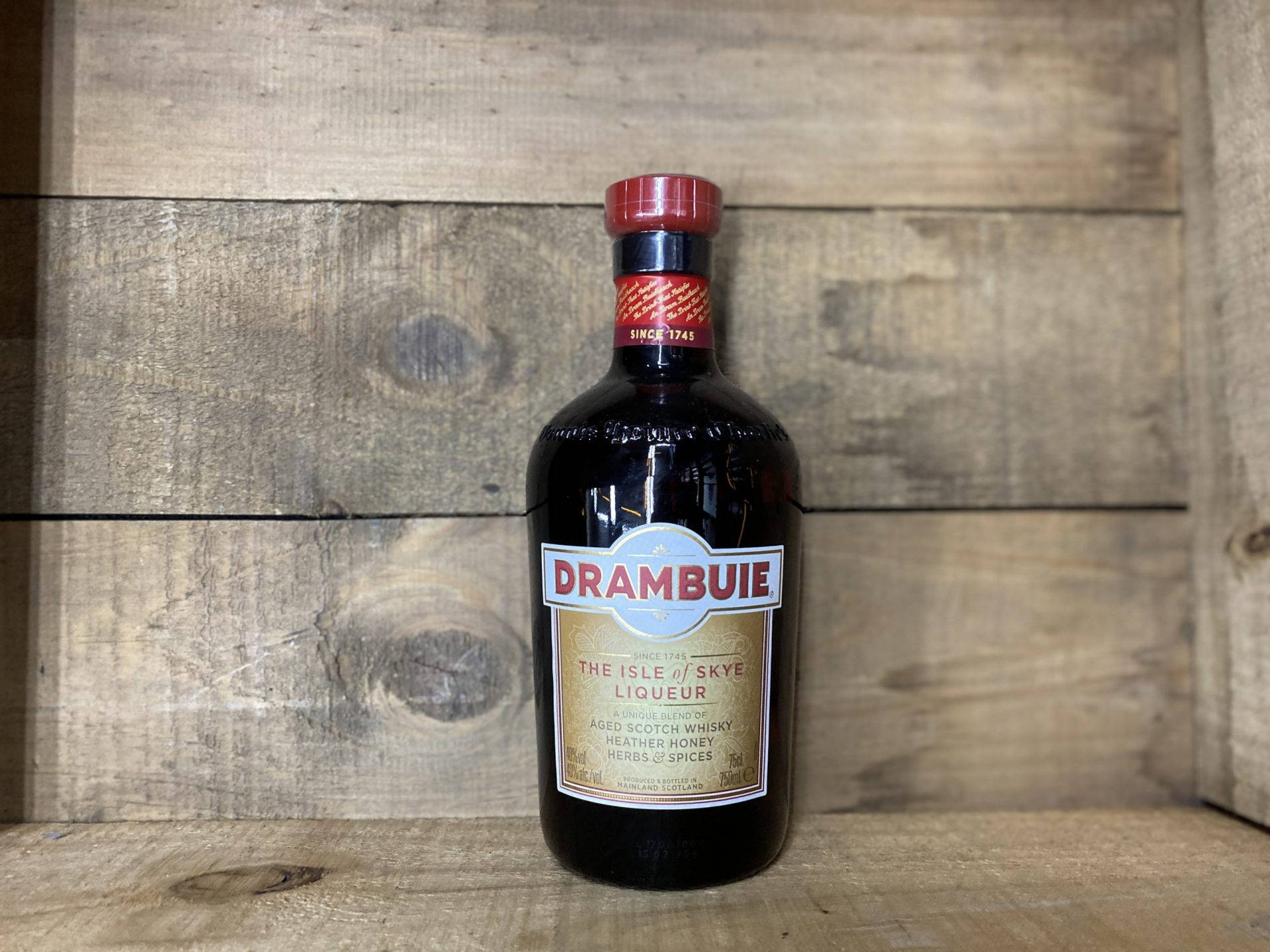 alcohol 桌布 壁紙 — 一瓶深色 Drambuie 利口酒，紅色瓶蓋，置於質樸木板上，背景為相配的木牆。