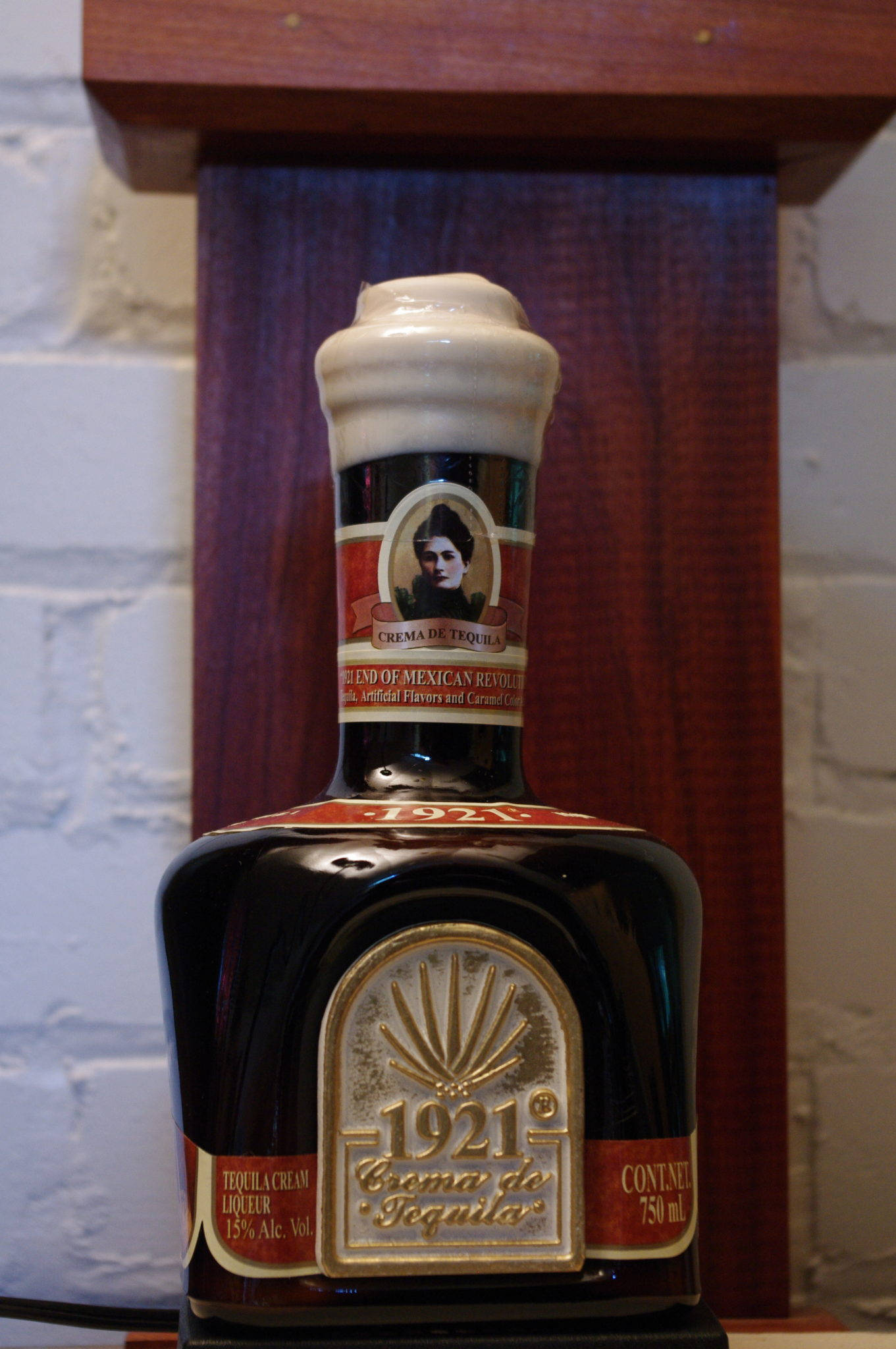 drinks 桌布 壁紙 — 一瓶深色玻璃瓶裝的1921 Crema de Tequila，配有奶油色瓶蓋，放在白色磚牆前的木架上。