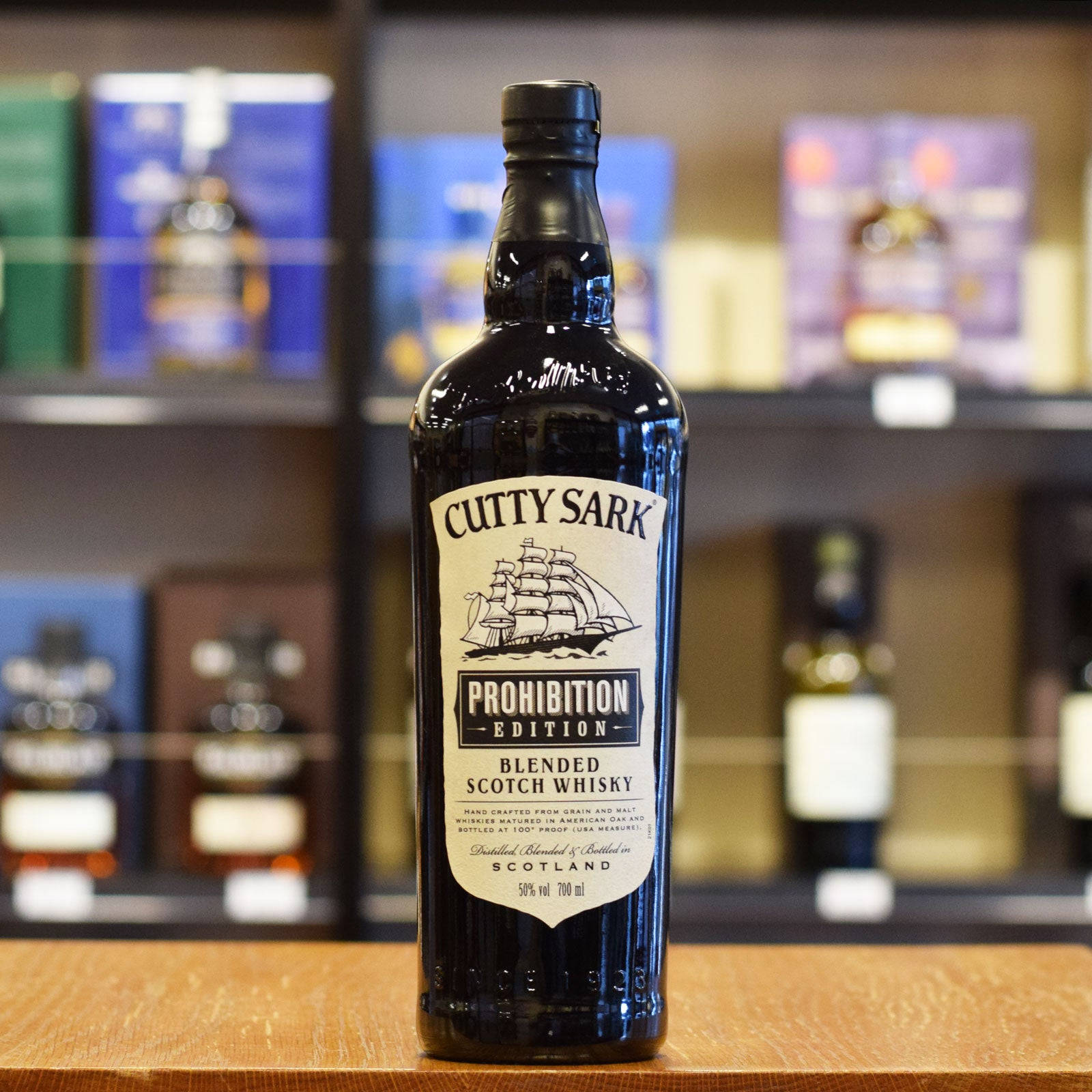 alcohol 桌布 壁紙 — 一瓶深色的Cutty Sark Prohibition Edition威士忌醒目地放在木製櫃檯上，背景是其他烈酒的模糊酒架。