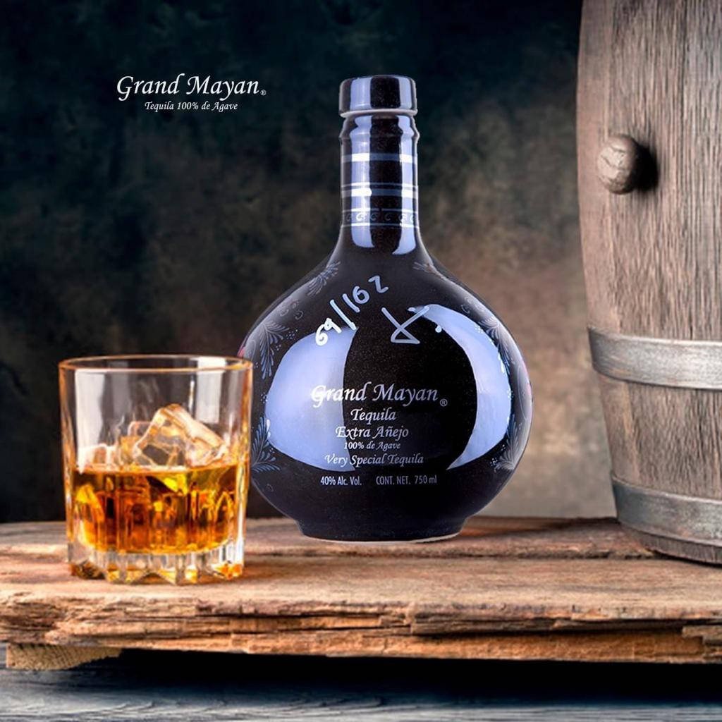 alcohol 桌布 壁紙 — 一瓶深色的Grand Mayan Extra Añejo龍舌蘭酒放在一個琥珀色液體的玻璃杯旁邊，置於一個桶旁邊的質樸木板上。