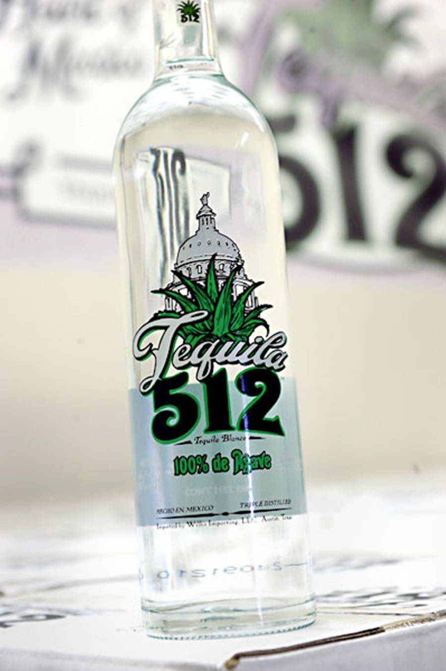 drinks 桌布 壁紙 — 一瓶清晰玻璃瓶裝的Tequila 512，帶有綠色標籤和龍舌蘭植物圖案，在模糊背景中清晰對焦。