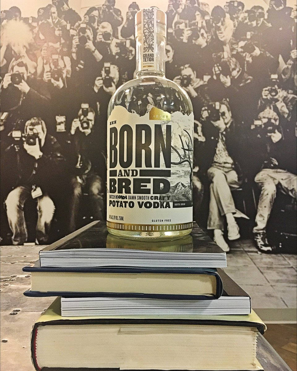 books 桌布 壁紙 — 一瓶清澈的 Born and Bred 馬鈴薯伏特加放在一堆書本上，背景是攝影師的黑白照片。