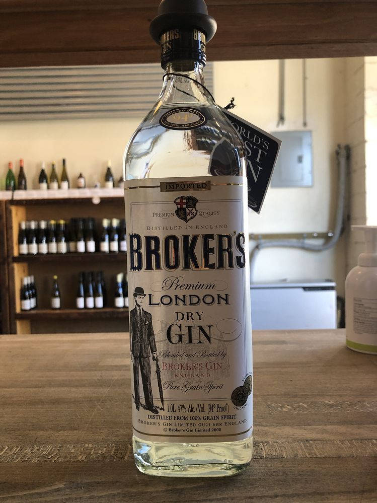 bottle 桌布 壁紙 — 一瓶清澈的 Broker's Premium London Dry Gin 放在一個木製吧檯上，背景是擺滿酒瓶的酒架。