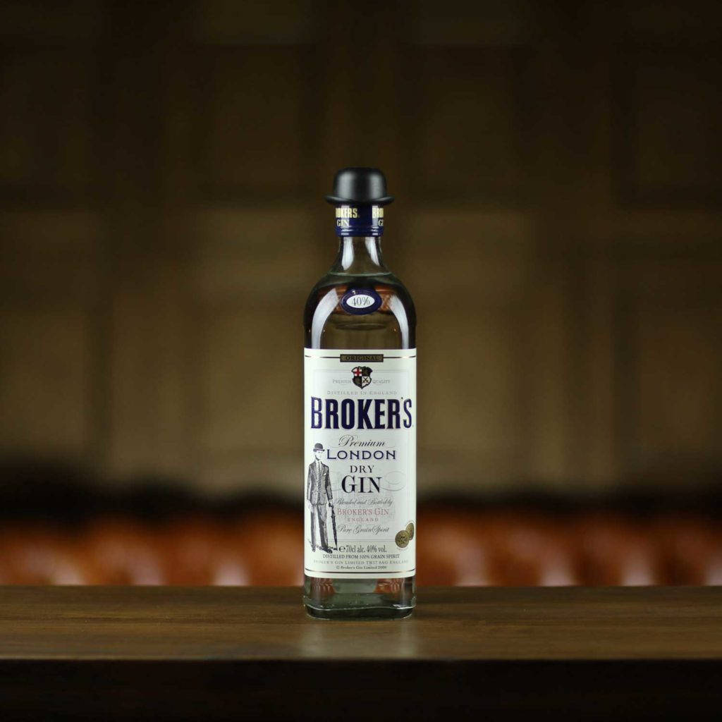 bottle 桌布 壁紙 — 一瓶清澈的 Brokers Premium London Dry Gin 酒瓶居中放置在深色木質吧檯上，背景為模糊的暖色調。