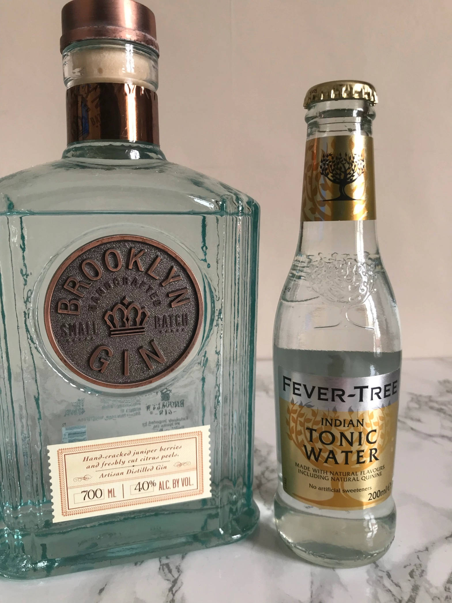 alcohol 桌布 壁紙 — 一瓶清澈的 Brooklyn Small Batch Gin 和一瓶 Fever-Tree Indian Tonic Water 並排放在大理石表面上。
