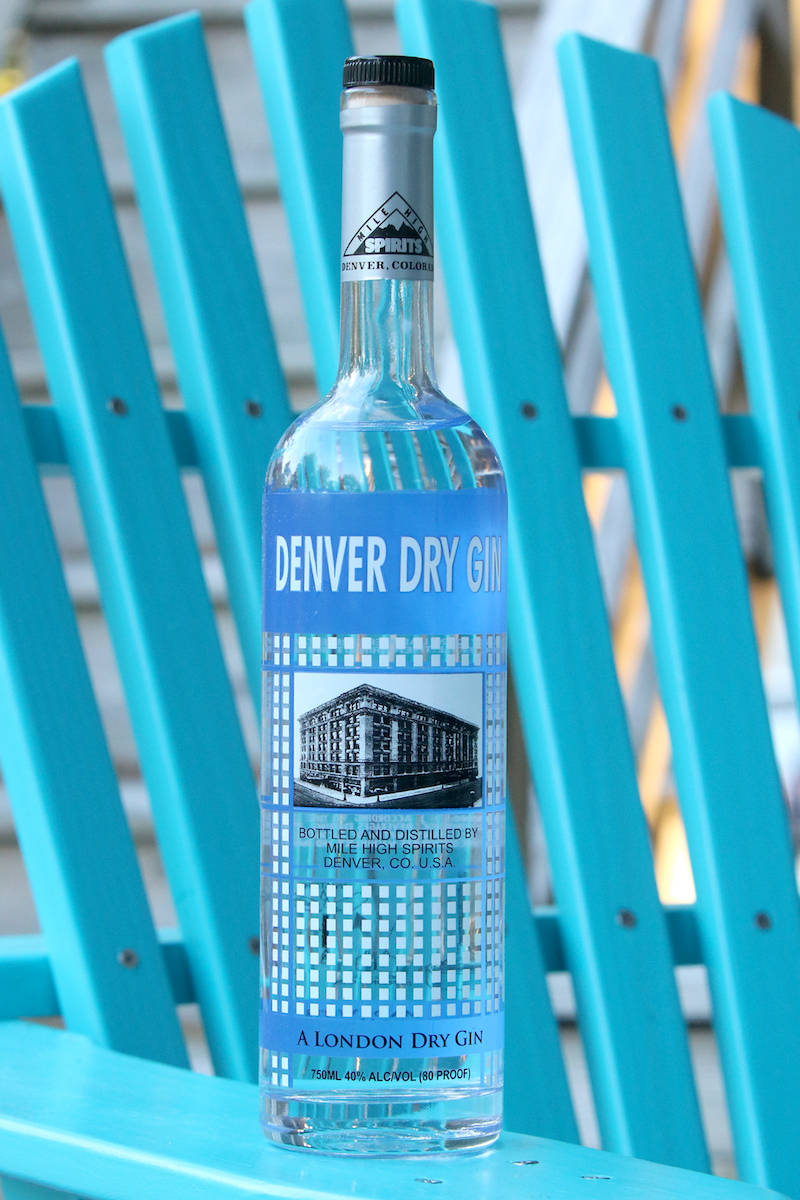 alcohol 桌布 壁紙 — 一瓶清澈的 Denver Dry Gin 放在戶外一張充滿活力的藍綠色木椅上。