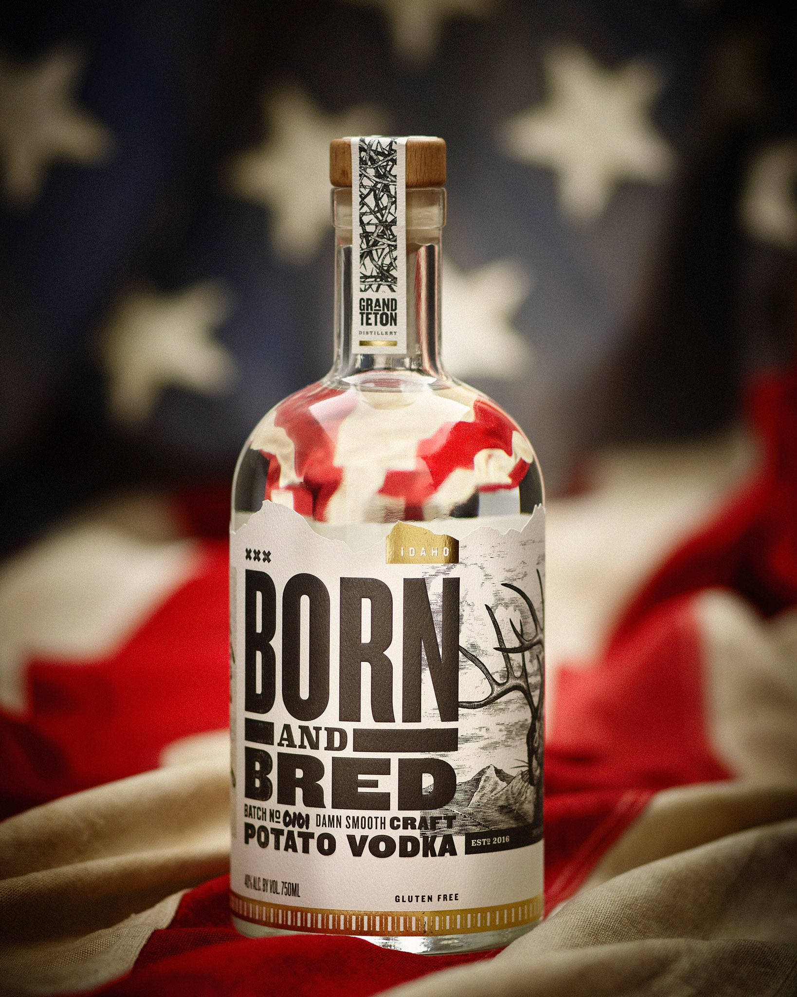 USA Flag 桌布 壁紙 — 一瓶清澈的Born and Bred馬鈴薯伏特加酒，醒目地放在模糊的美國國旗背景前。