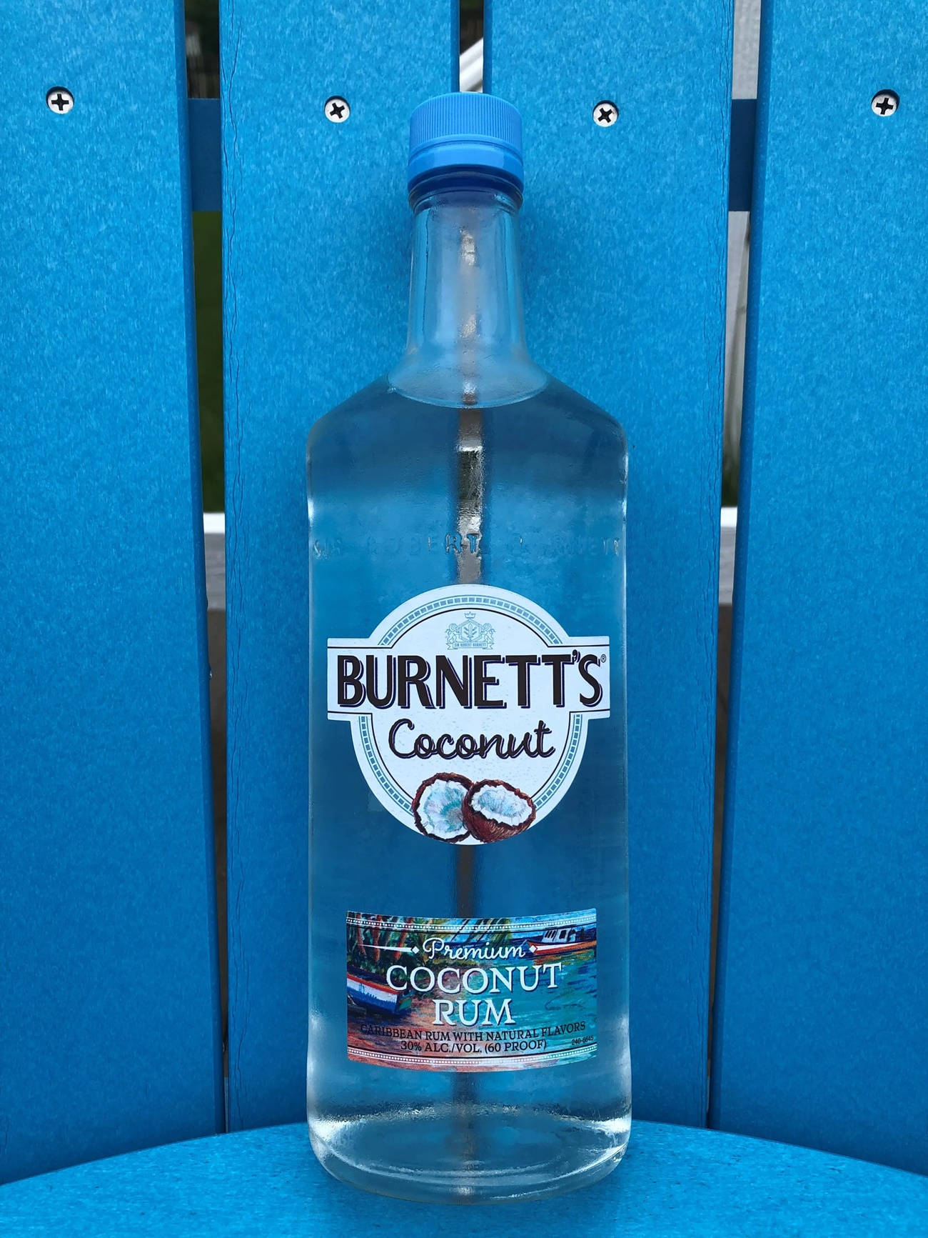drinks 桌布 壁紙 — 一瓶清澈的Burnett's Coconut Rum放在戶外一張亮藍色木椅的正中央。