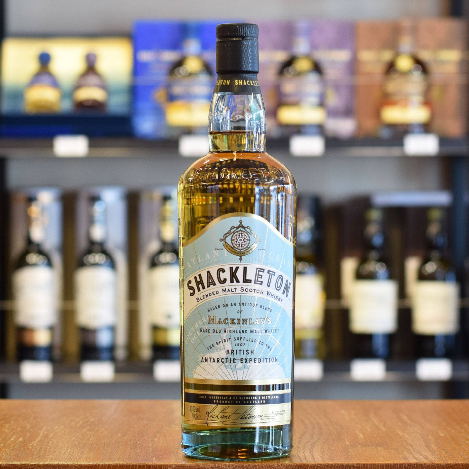 Drink 桌布 壁紙 — 一瓶清澈的Shackleton Blended Malt Scotch Whisky醒目地放在木製櫃檯上，背景是模糊的其他酒類貨架。