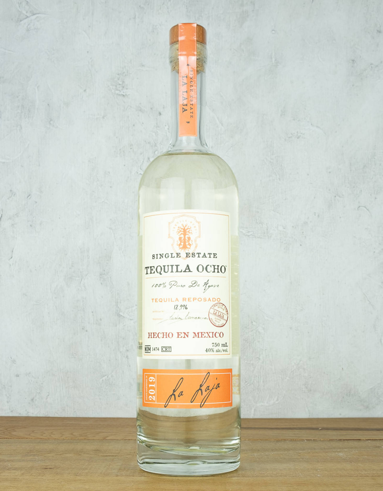 bottle 桌布 壁紙 — 一瓶清澈的Tequila Ocho reposado直立於木質表面上，背景是帶紋理的灰色牆壁。