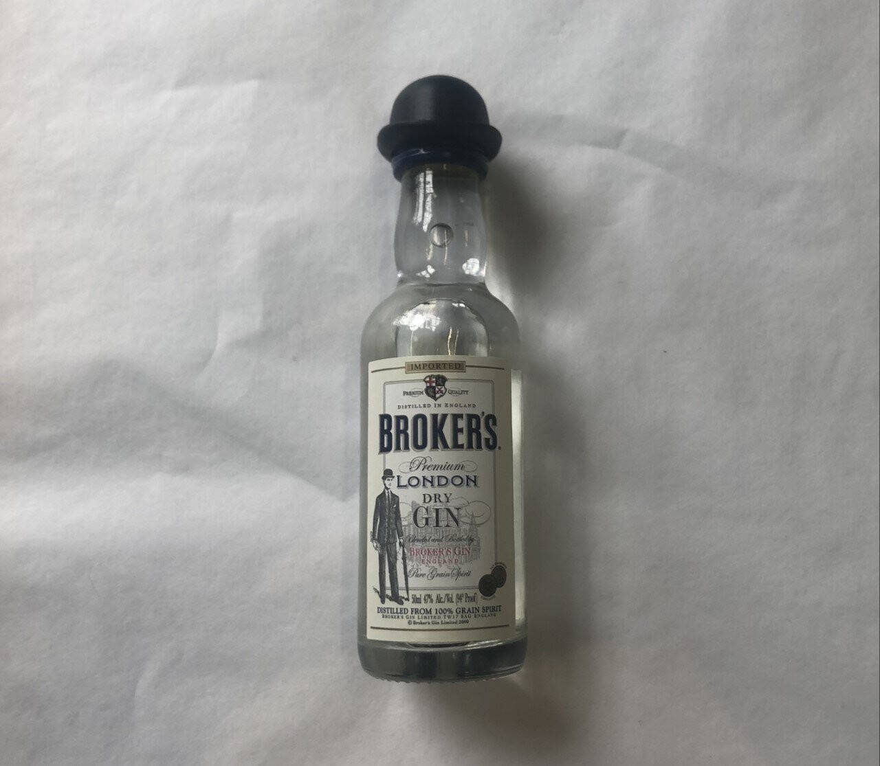 small 桌布 壁紙 — 一瓶清澈的玻璃瓶裝 Broker's Premium London Dry Gin，帶黑色瓶蓋，居中放置在皺巴巴的白色布料背景上。
