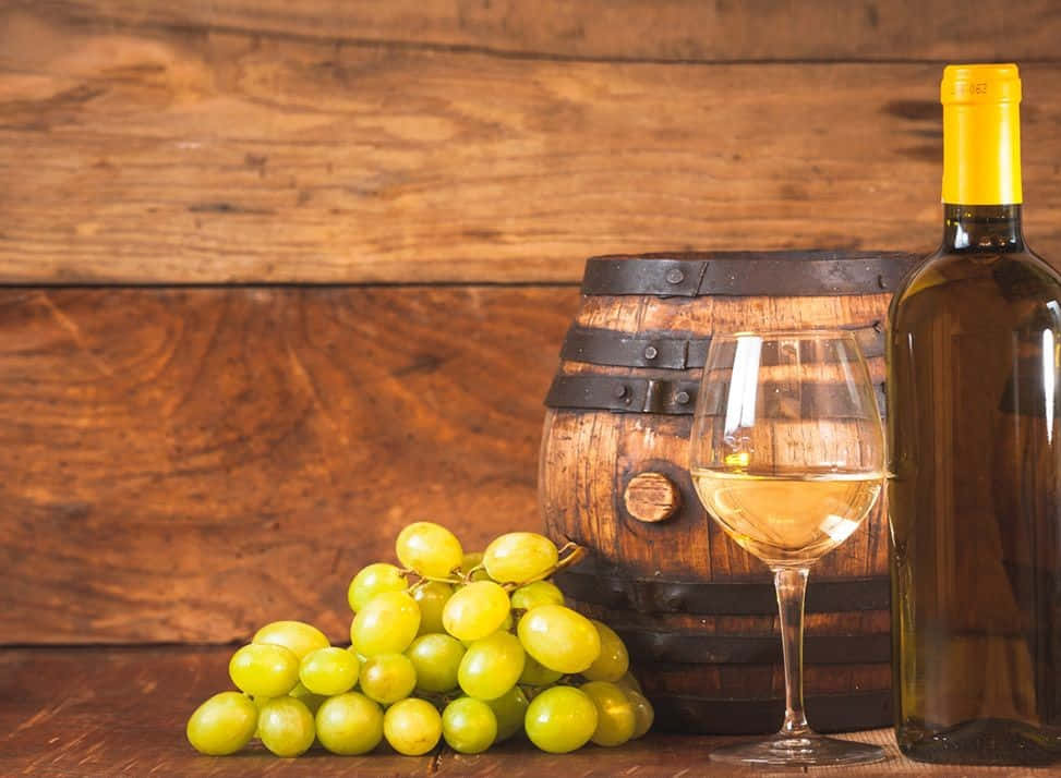 White Wine 桌布 壁紙 — 一瓶白酒和一個酒杯放在一個木桶和一串青葡萄旁邊，置於質樸的木桌上。