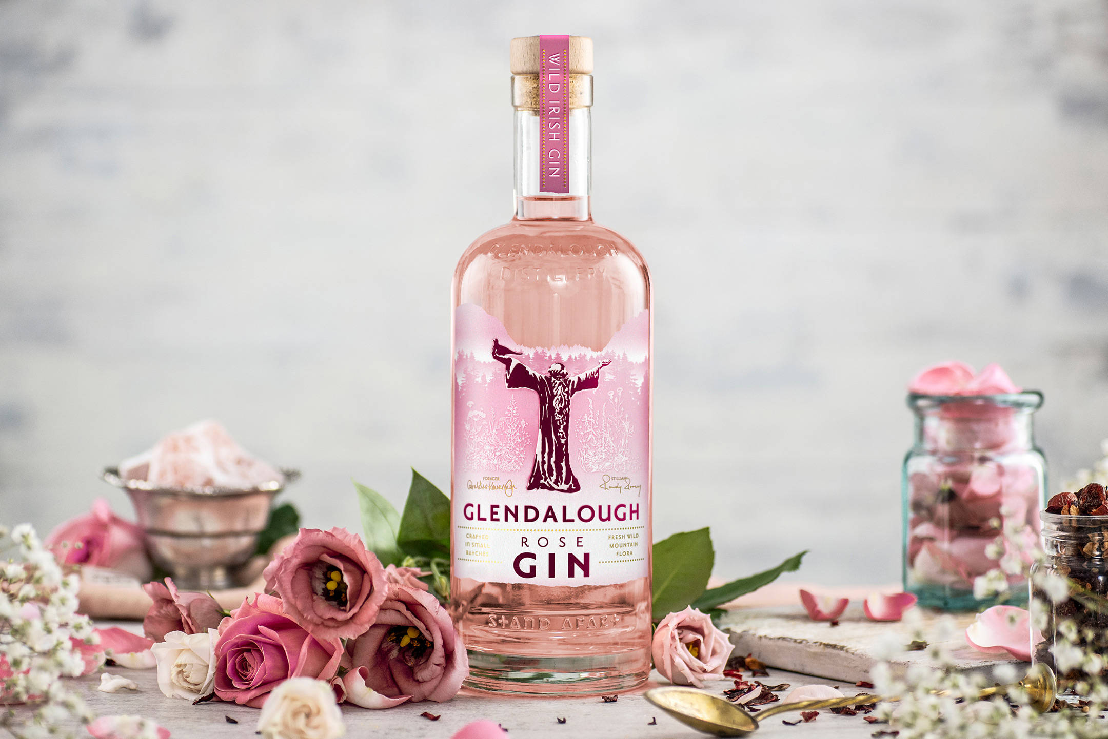 Gin 桌布 壁紙 — 一瓶粉紅玫瑰琴酒優雅地站立，周圍是新鮮的粉紅玫瑰和植物裝飾，放在質樸的木質表面上。