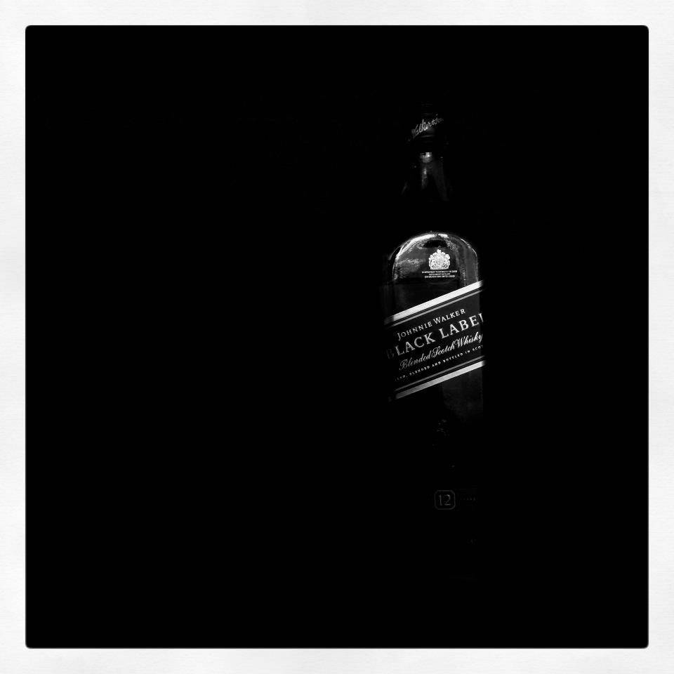 alcohol 桌布 壁紙 — 一瓶約翰走路黑牌威士忌在漆黑背景上以高對比度單色微弱發光。