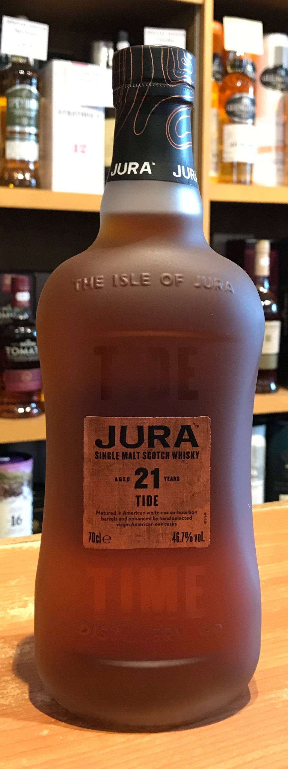 手機 桌布 壁紙 — 一瓶結霜的 Jura 21 年單一麥芽蘇格蘭威士忌放在木質表面上，背景有陳列其他烈酒的層架。