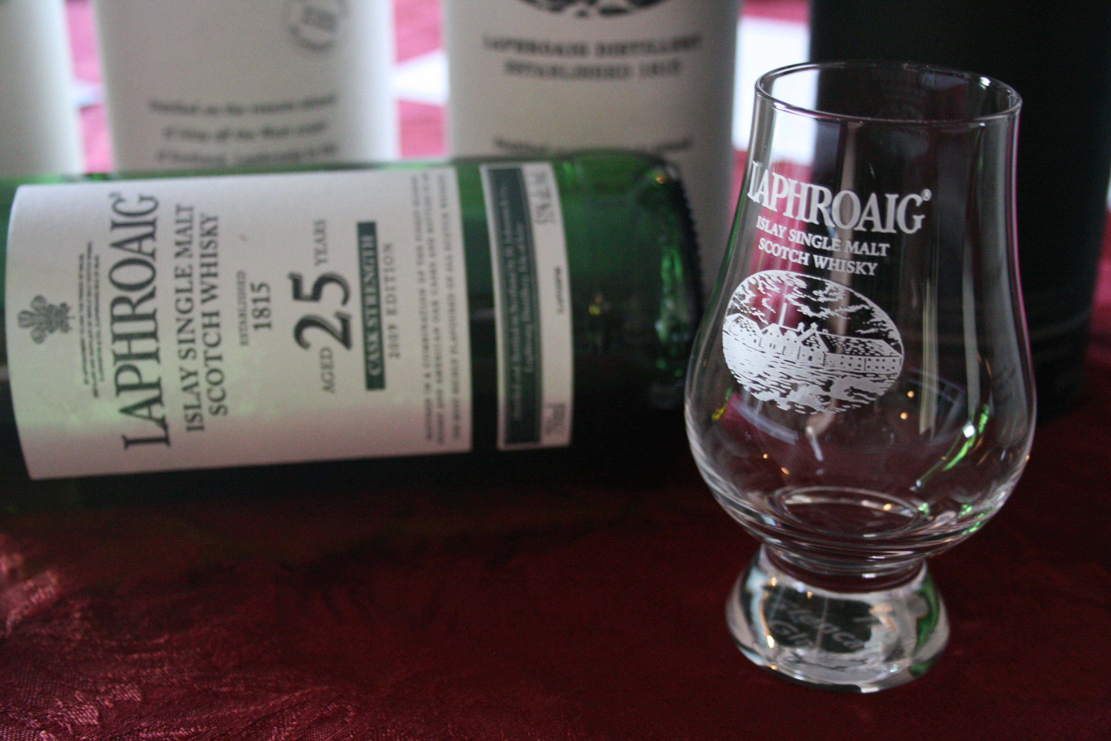 Best 桌布 壁紙 — 一瓶綠色Laphroaig 25年威士忌酒瓶連同其品牌品酒杯放在濃郁的紅色天鵝絨表面上。