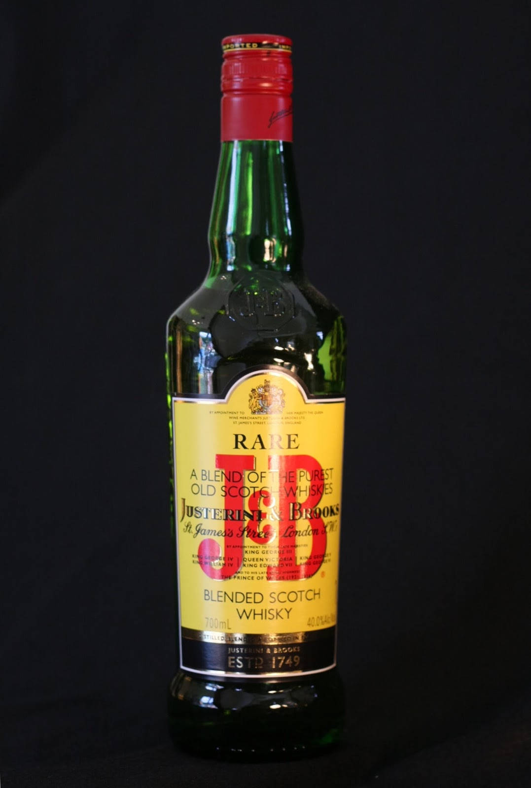 drinks 桌布 壁紙 — 一瓶綠色玻璃瓶的Justerini & Brooks Rare Blended Scotch Whisky，在黑色背景前，帶有紅色瓶蓋和黃色標籤。