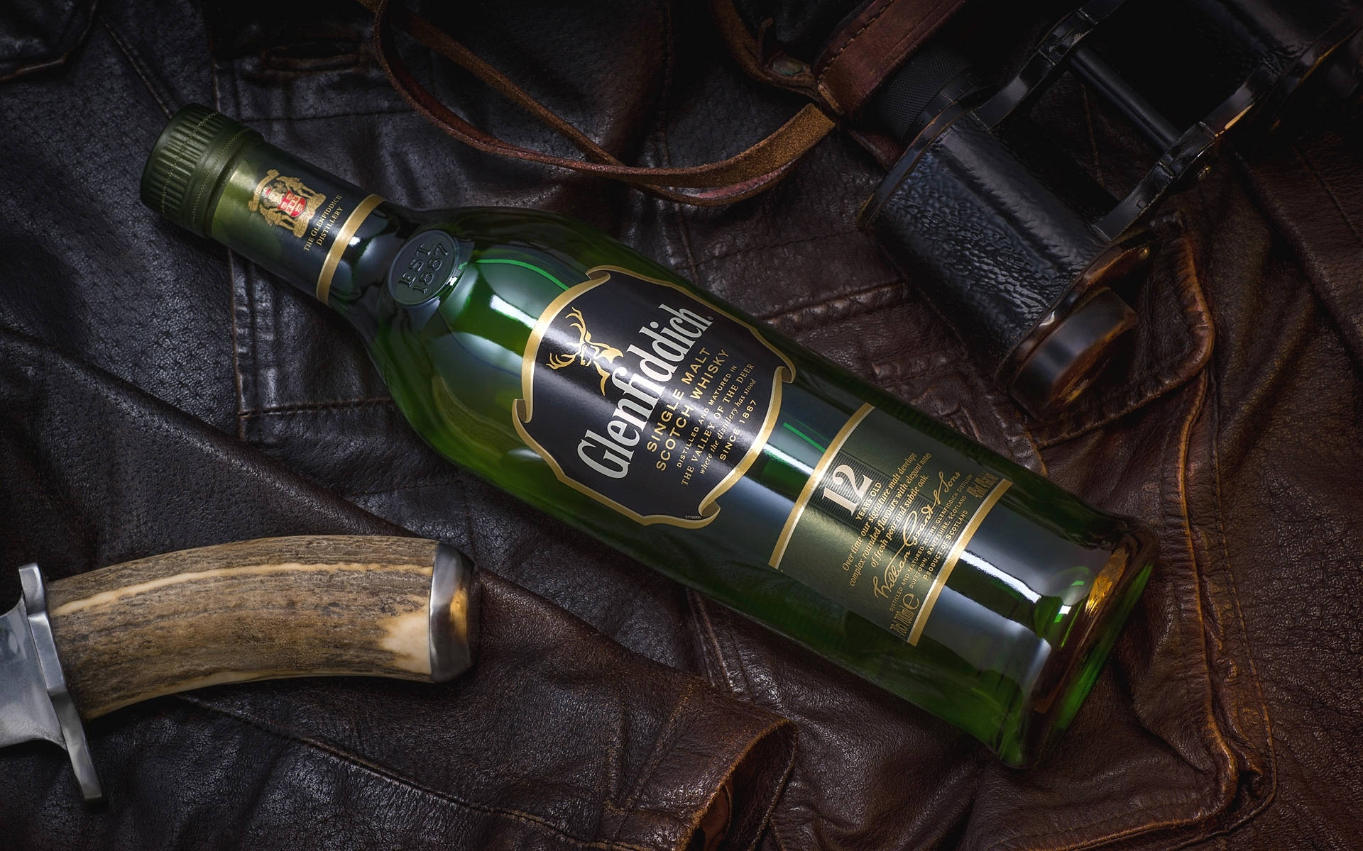 alcohol 桌布 壁紙 — 一瓶綠色的 Glenfiddich 12年威士忌酒瓶放在深色皮革上，旁邊有一把刀和望遠鏡。