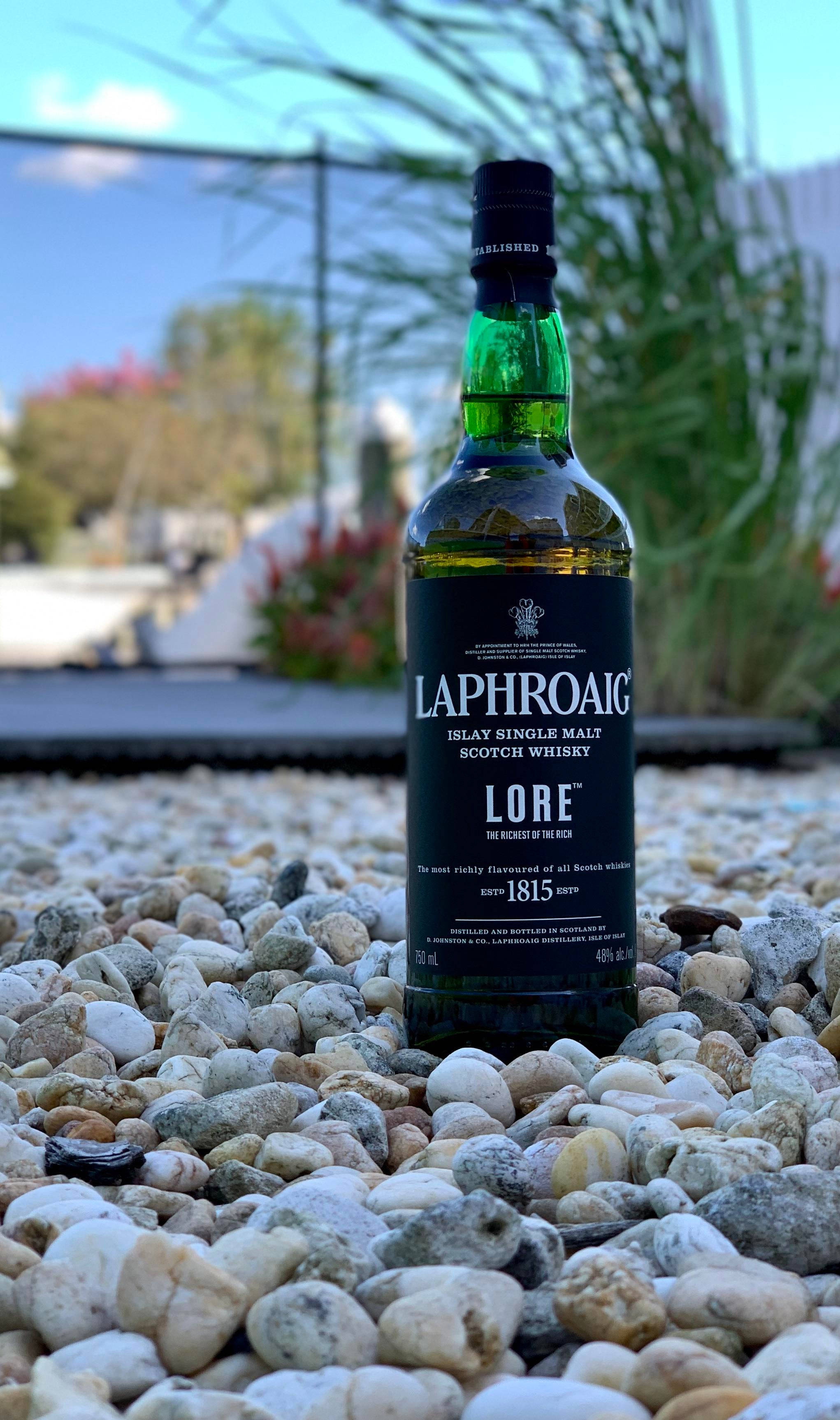 動態圖 桌布 壁紙 — 一瓶綠色的 Laphroaig Lore 威士忌在明亮的日光下，直立於平滑的白色和灰色鵝卵石上。